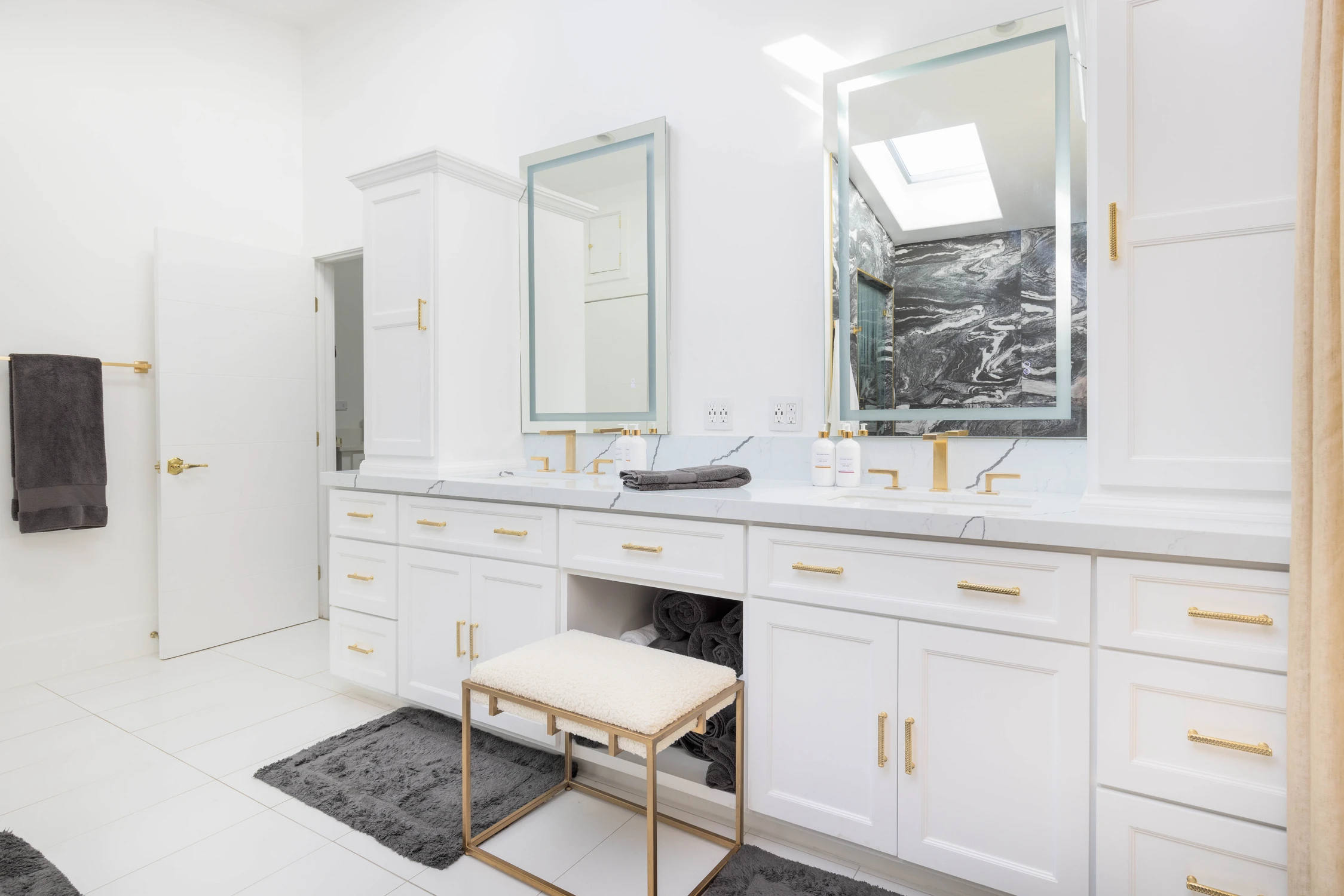 Master bathroom vanity with white cabinetry, gold hardware, and bench