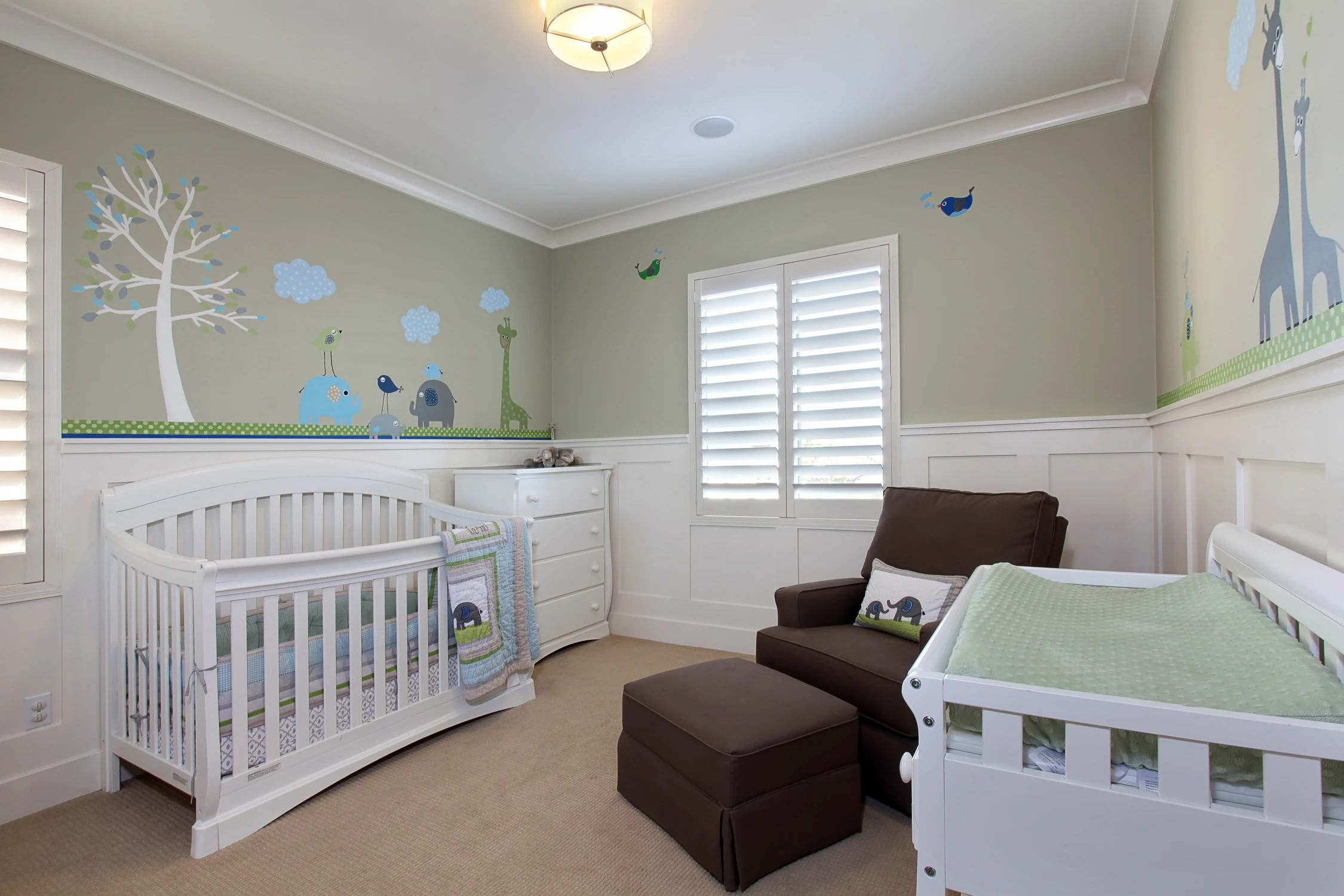 Nursery with white crib, green wall mural, and upholstered rocking chair