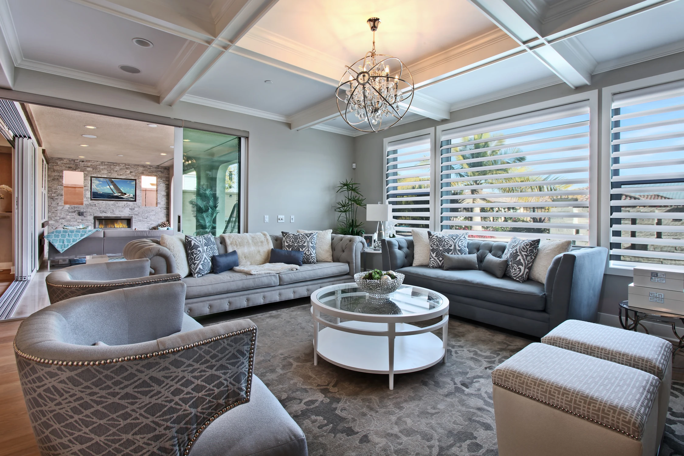 Family room with gray sectional, white shutters, and round glass coffee table