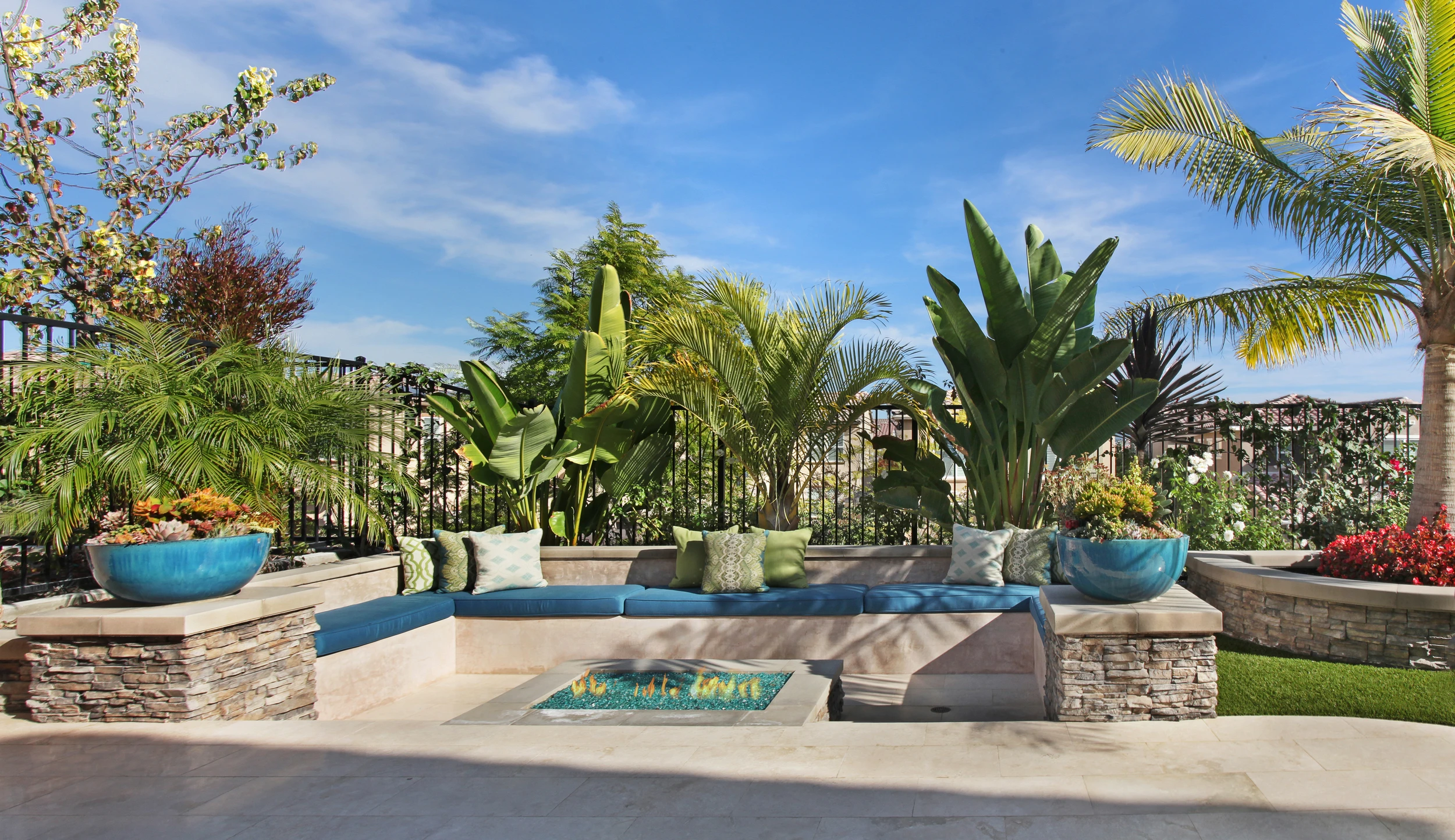 Sunken outdoor fire pit surrounded by palm trees and low stone wall