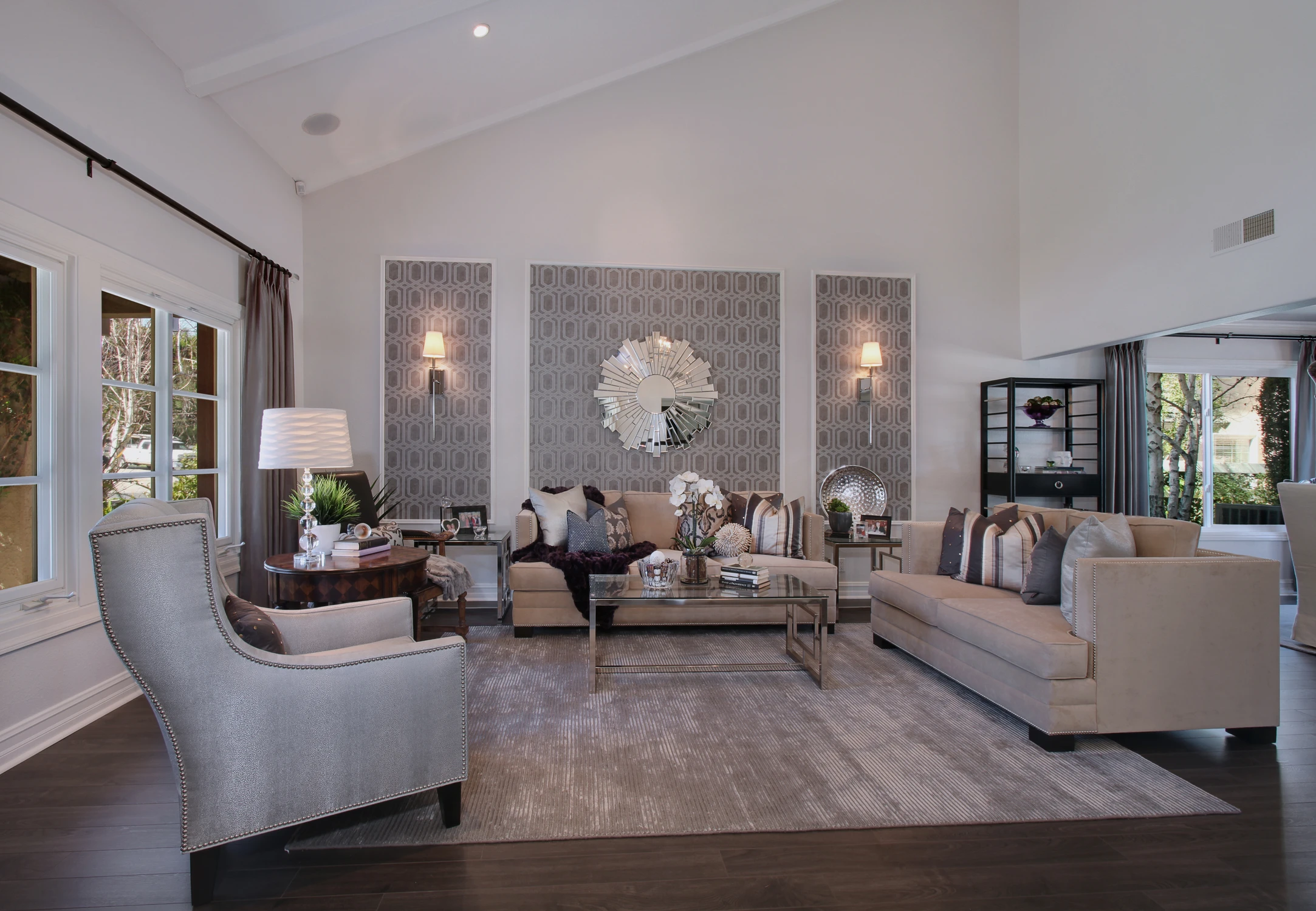 Formal living room with patterned wall panels, neutral sofas, and round mirror