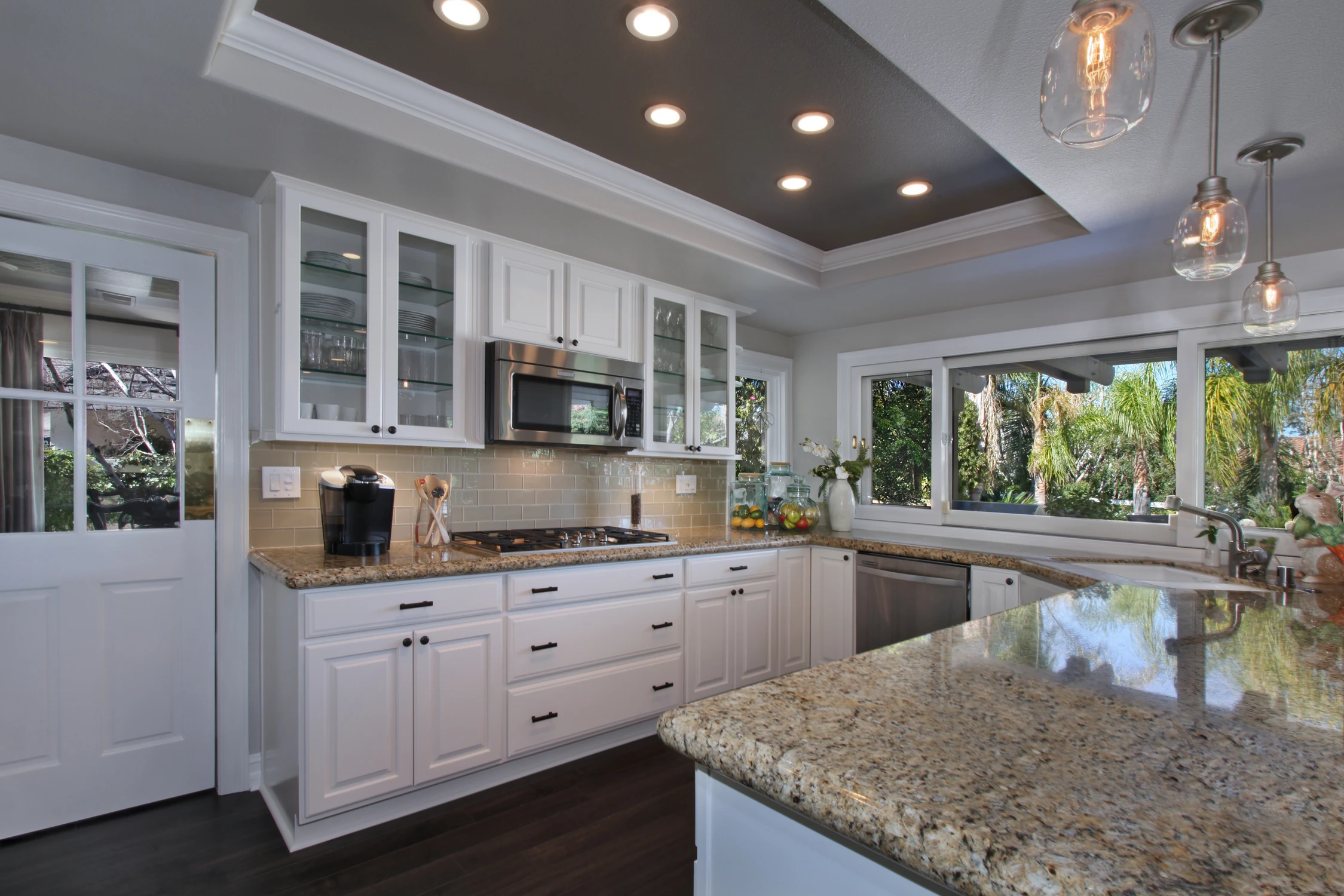 White kitchen with large stone island, glass cabinetry, and recessed ceiling