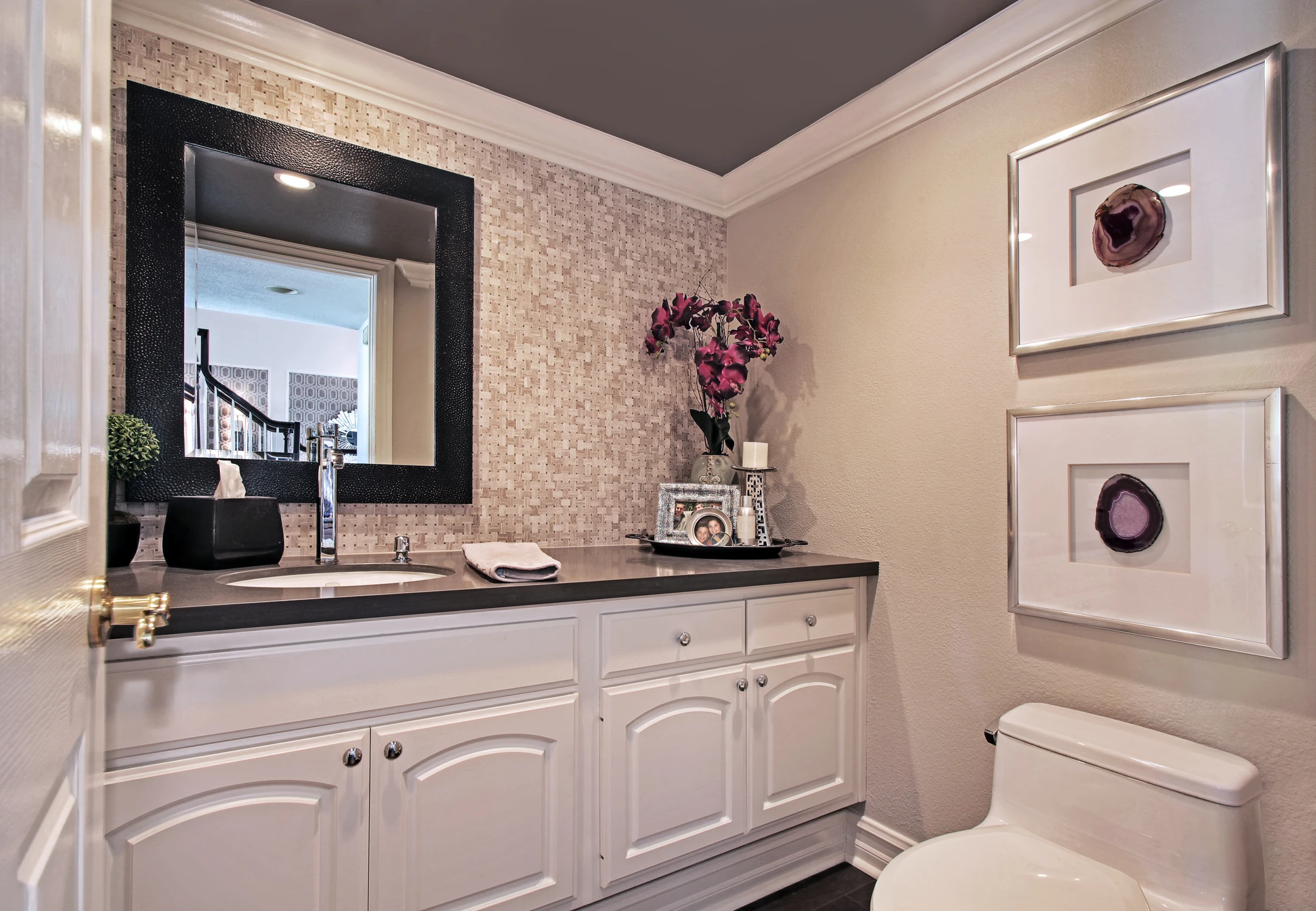 Powder room with curved white vanity, dark mirror, and framed artwork