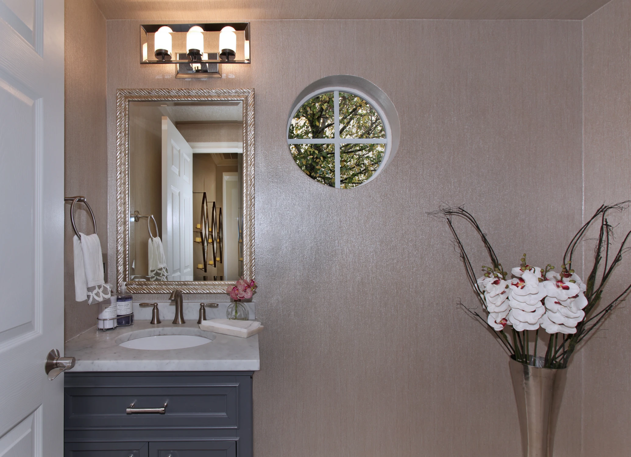 Powder room with dark vanity, round mirror, and patterned wall covering