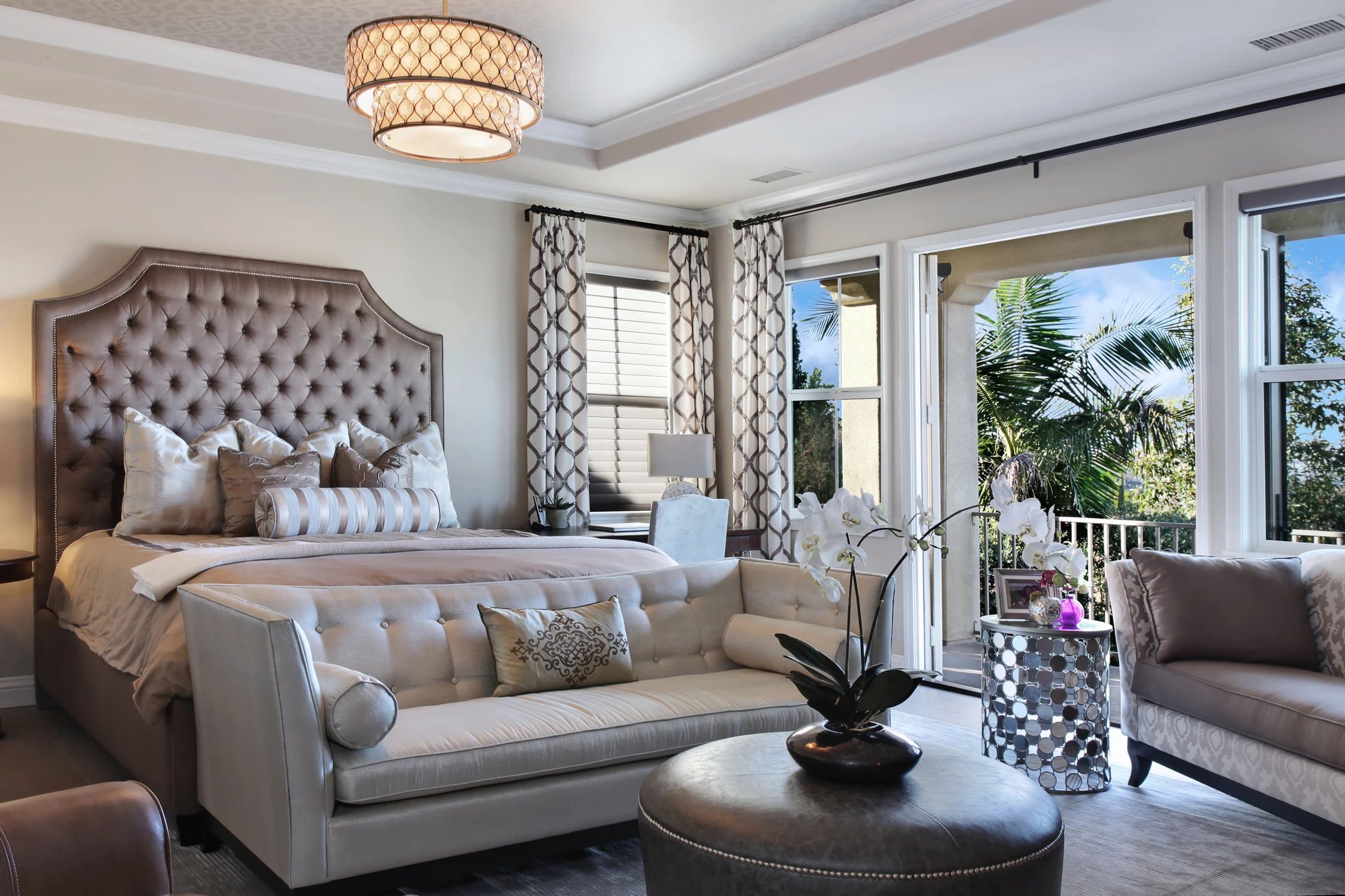 Bedroom with tall tufted headboard, pale seating, and balcony doors