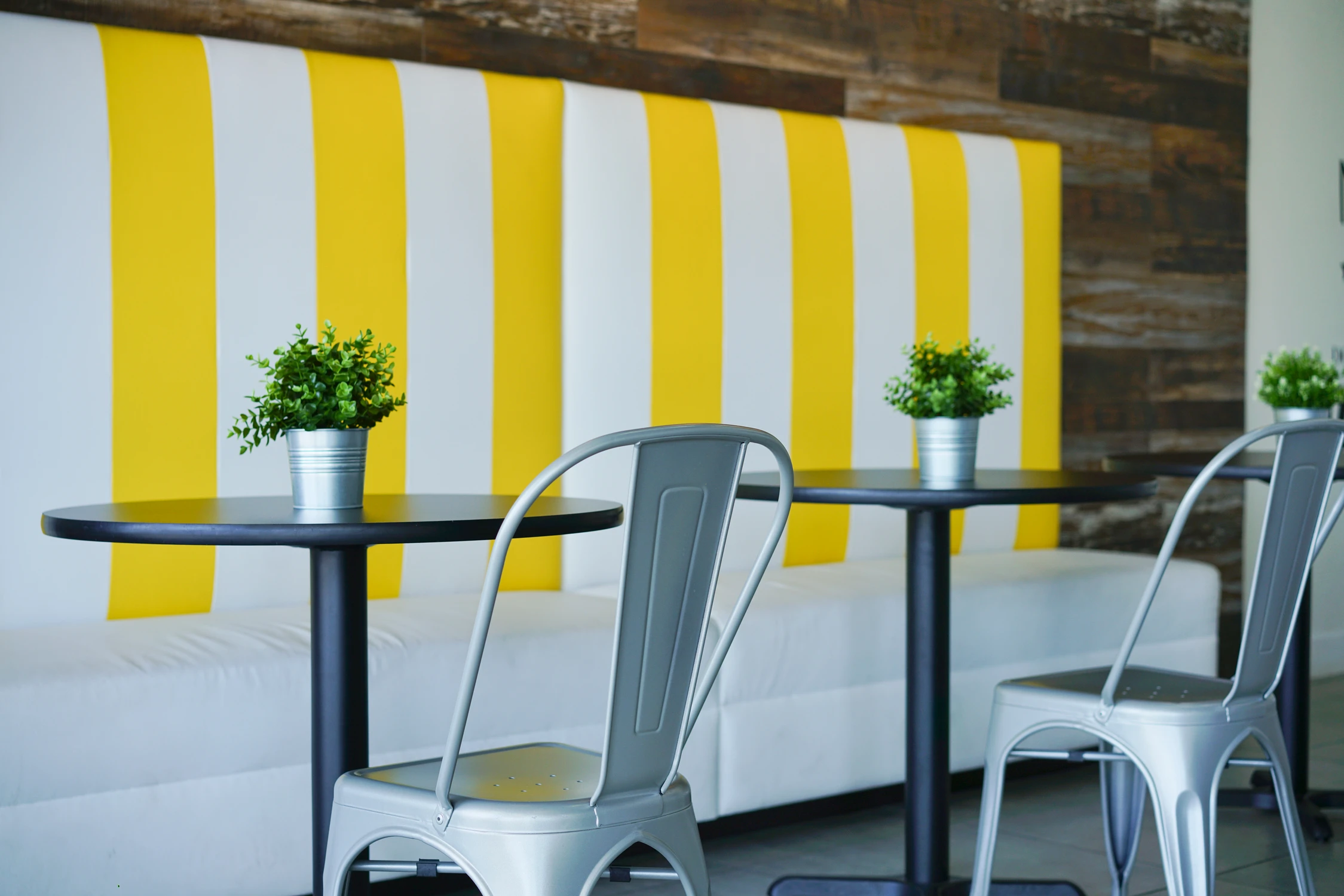 Café tables and metal chairs beside yellow striped banquette