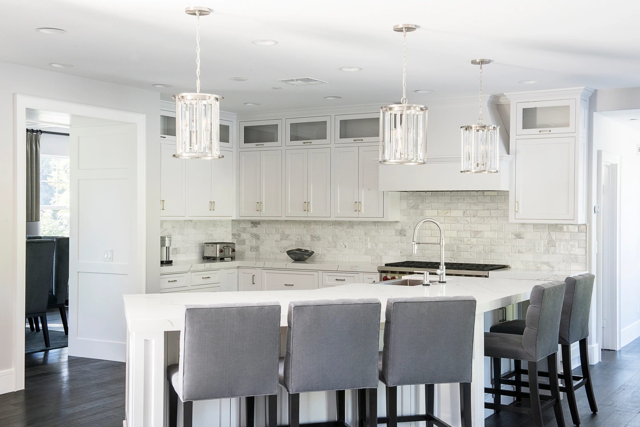 White kitchen island with gray upholstered stools and glass pendants