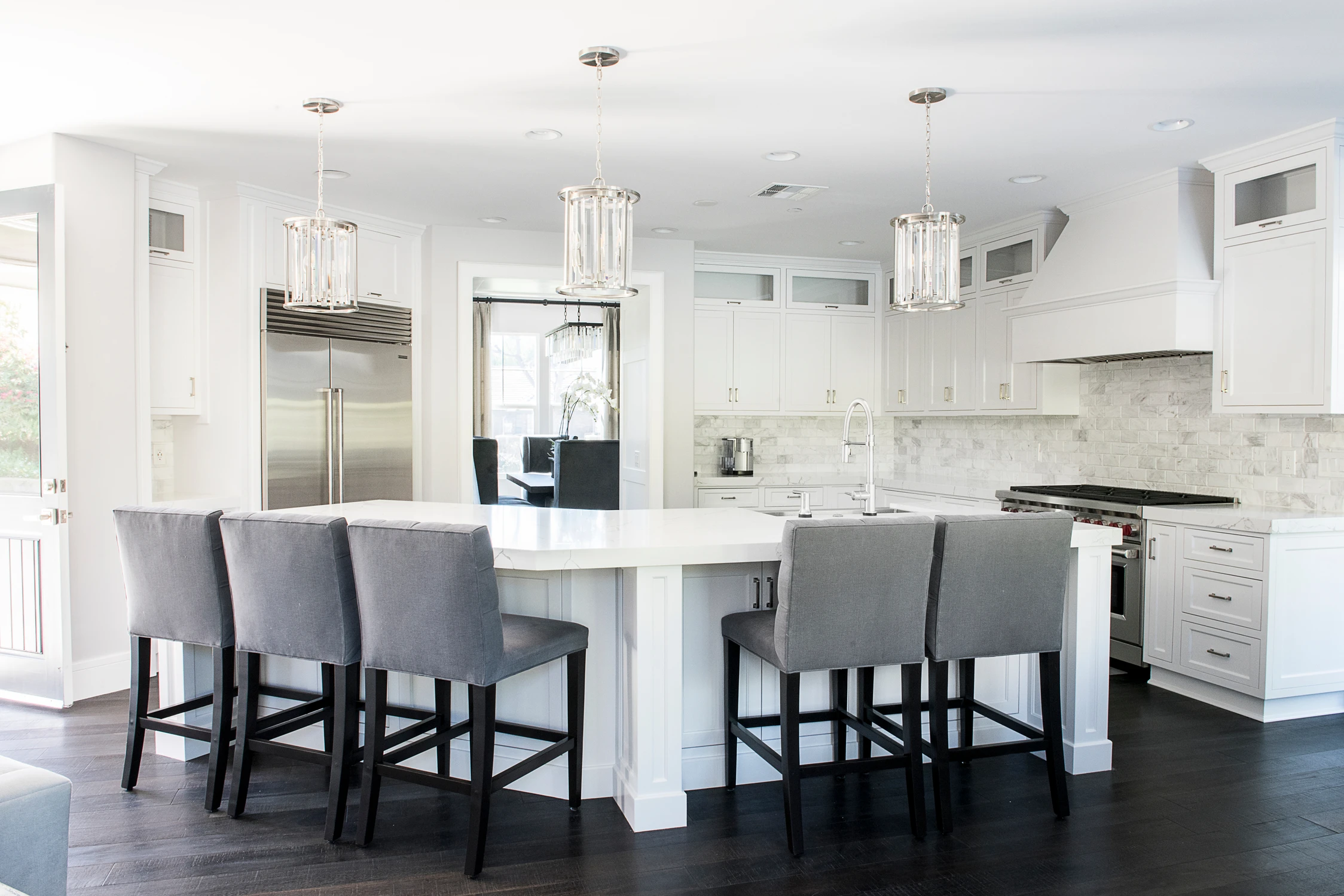 White kitchen with gray bar stools, marble island, and glass pendants