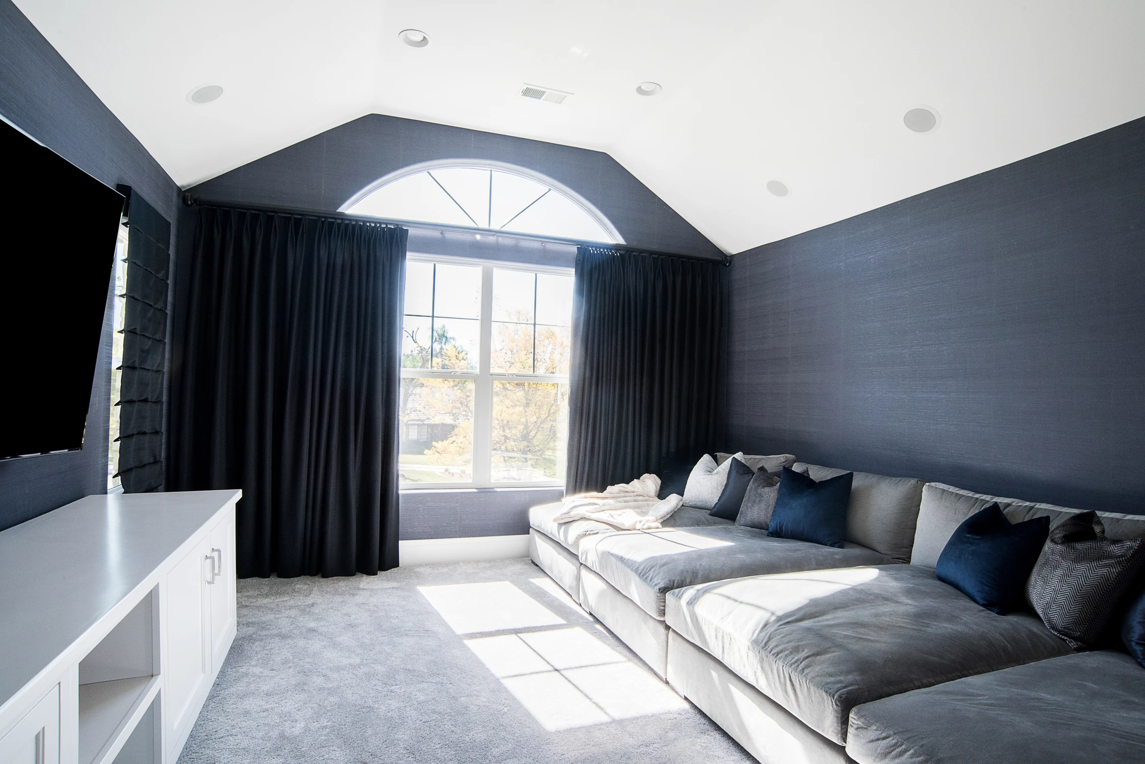 Media room with gray sectional, navy walls, and blackout curtains