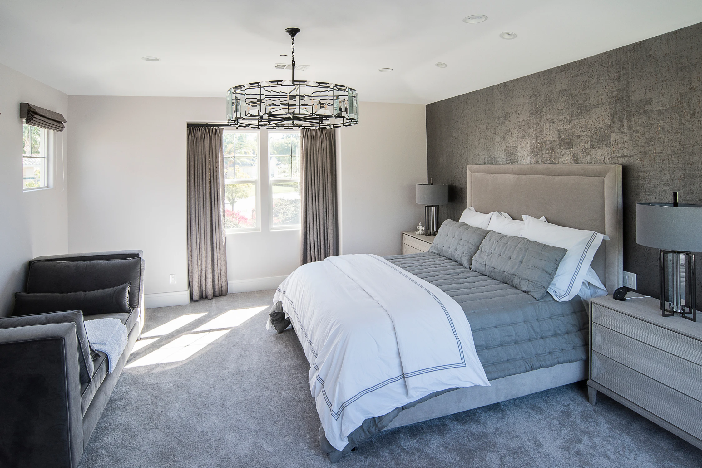 Primary bedroom with gray upholstered bed, textured accent wall, and chandelier