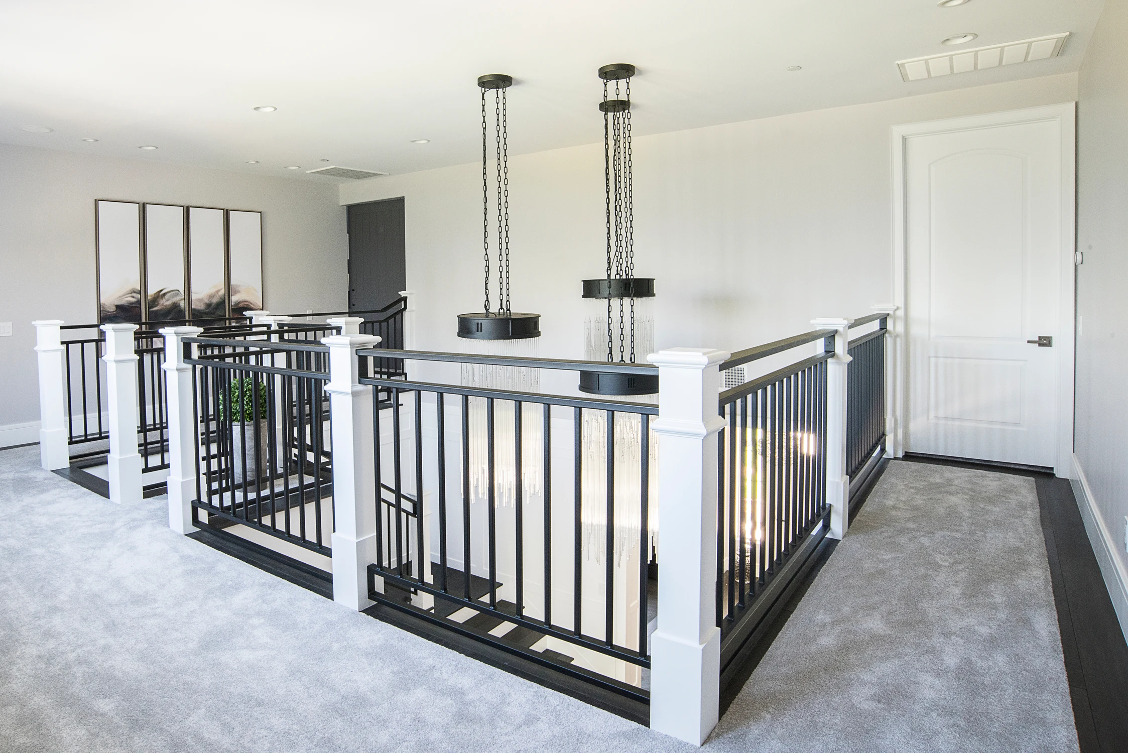 Upper landing with black railings, gray carpet, and chain pendants