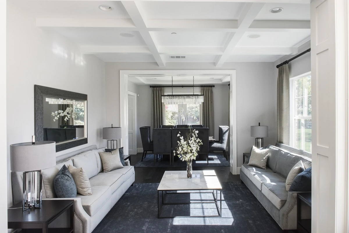 Formal living room with gray sofas, coffered ceiling, and dining room beyond