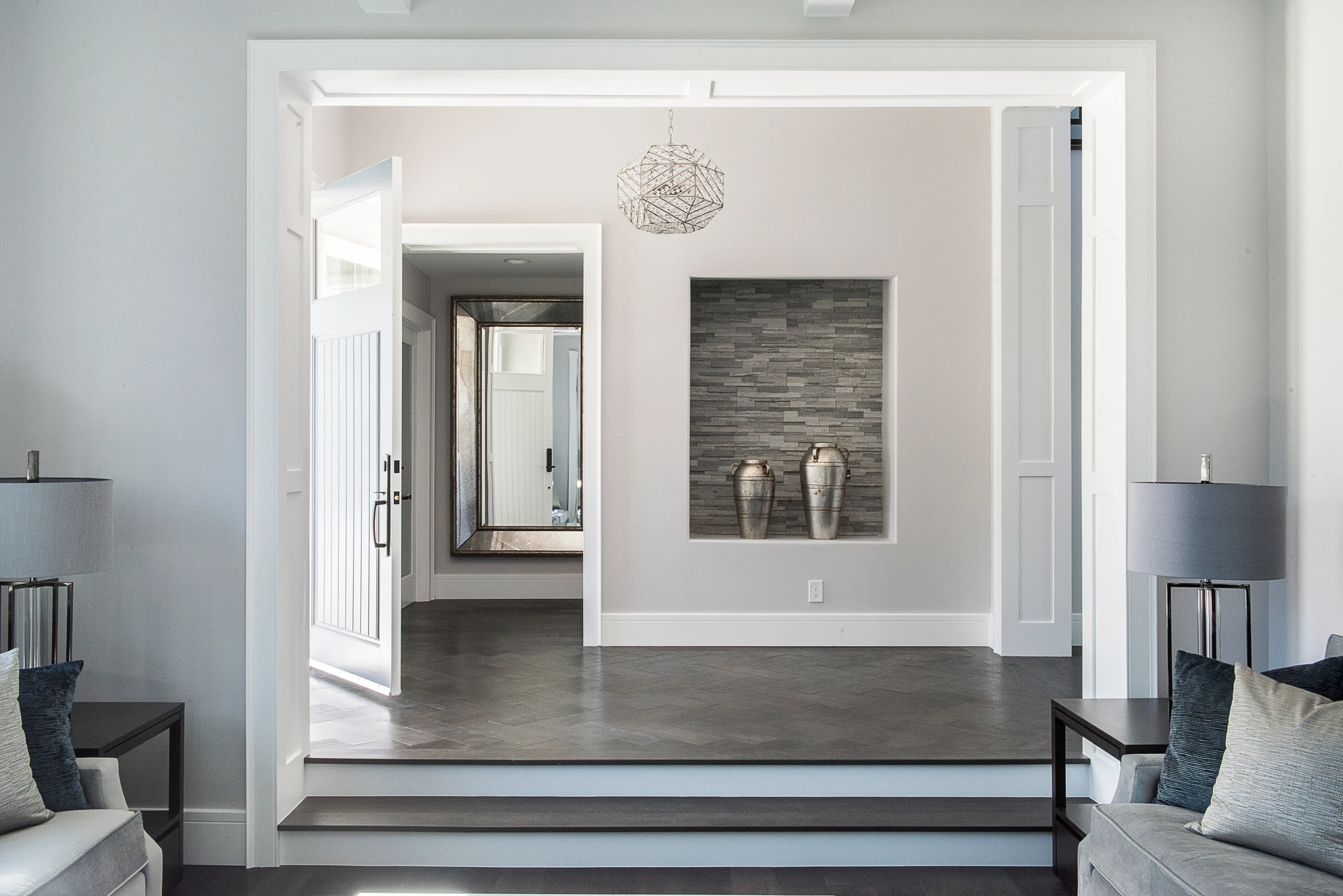 Foyer with open front door, black-framed mirror, and stone niche