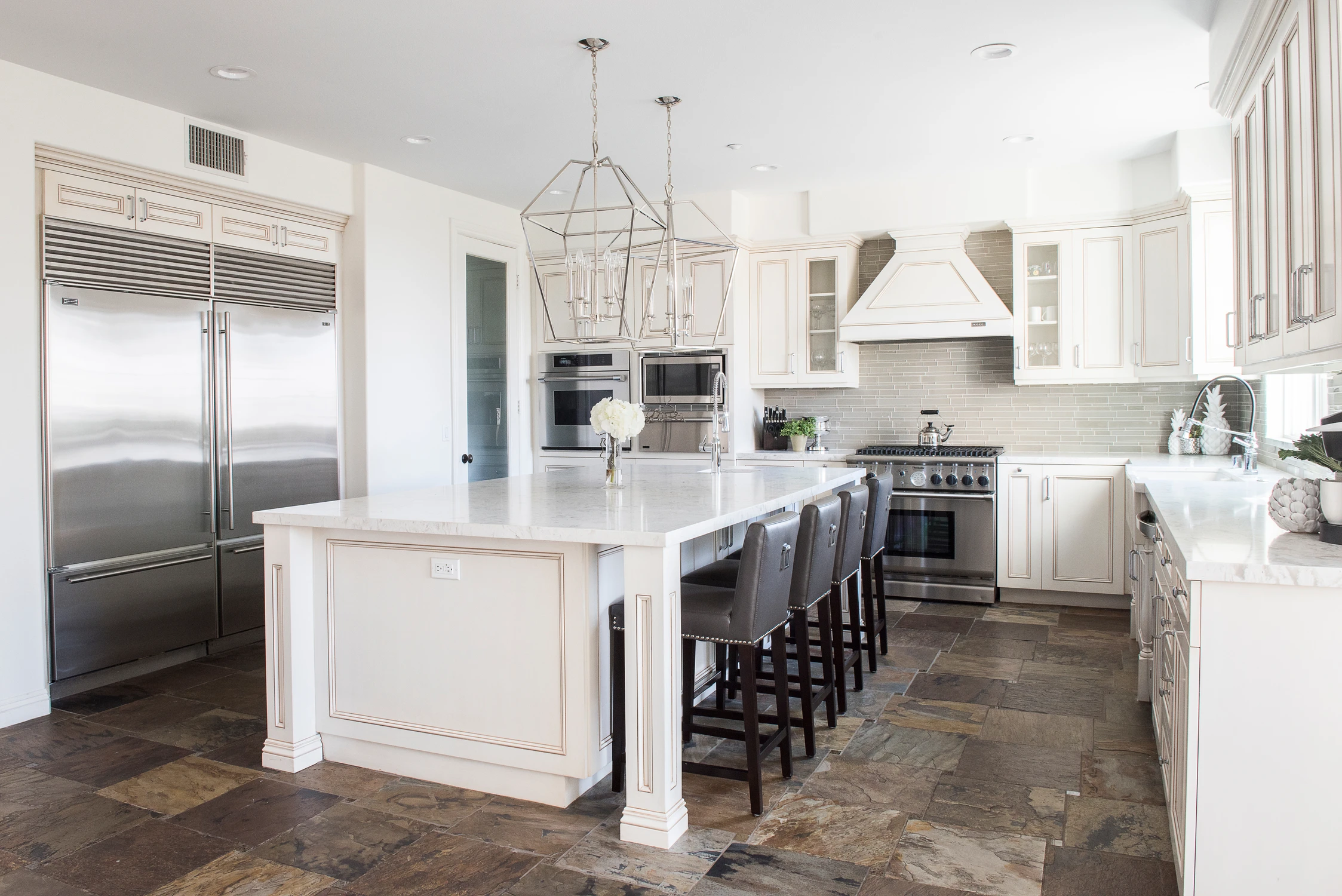 Kitchen island with dark stools and white cabinetry under pendant lights