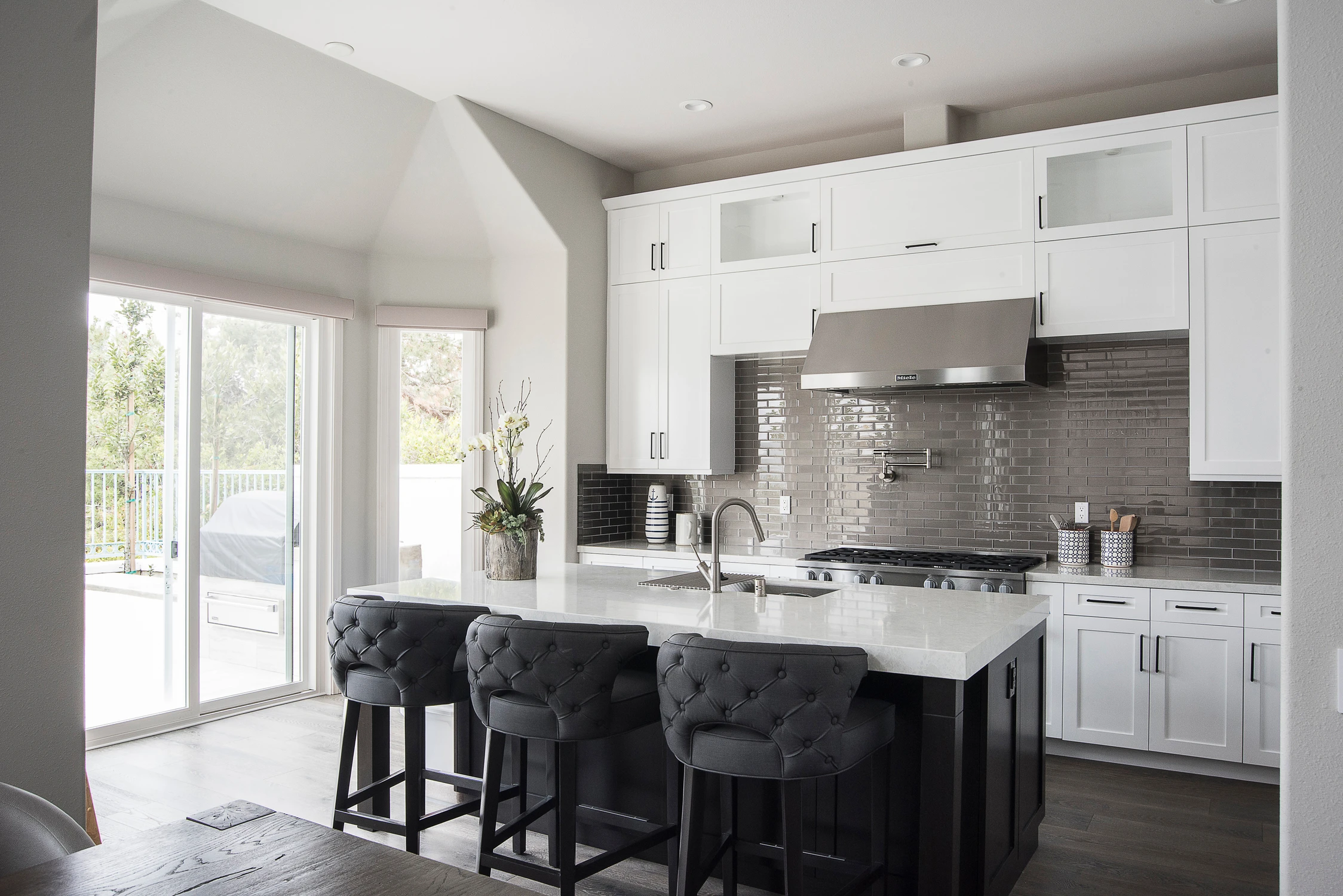 White kitchen with black island, dark stools, and patio doors