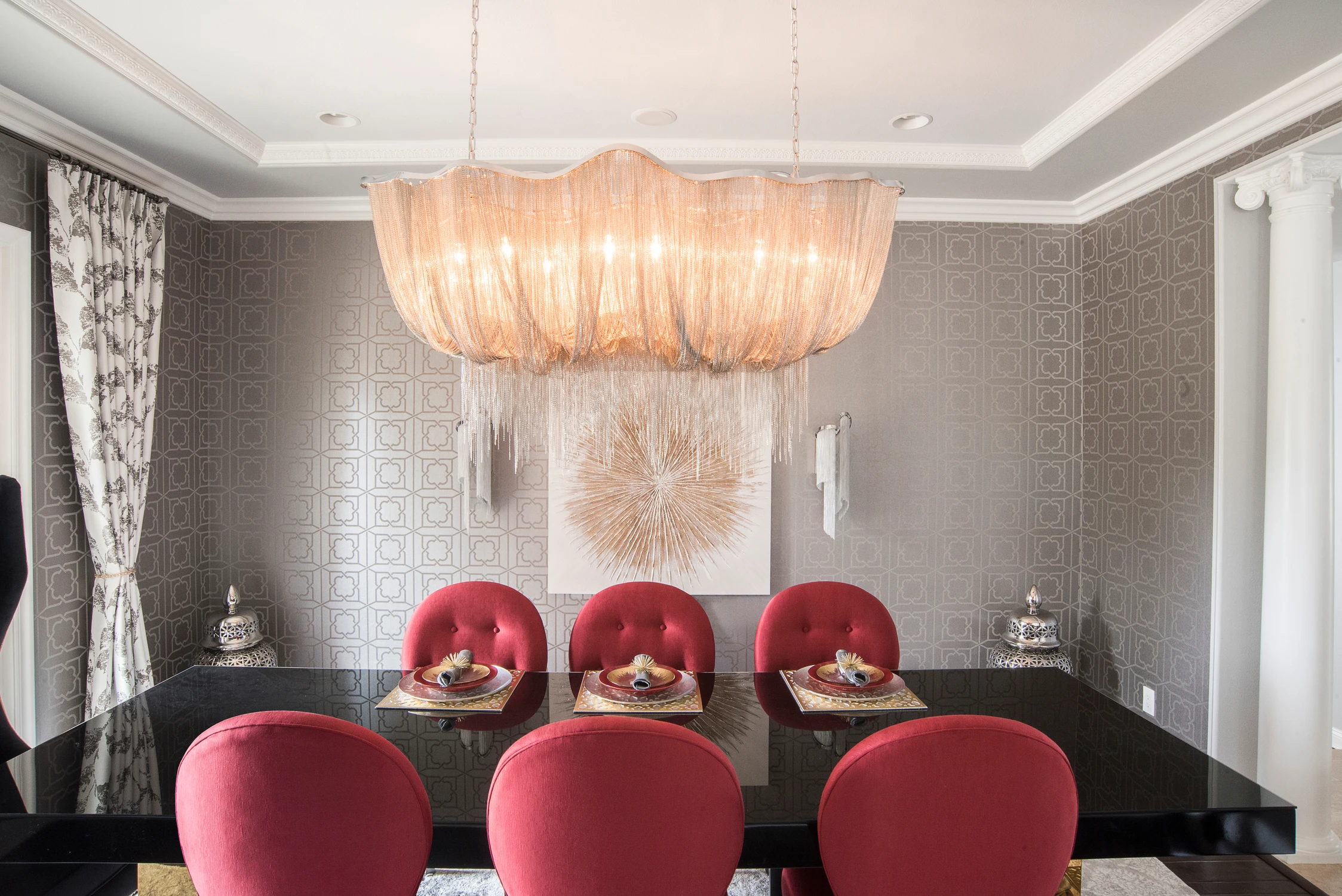 Dining room with red chairs, black table, and large sculptural chandelier