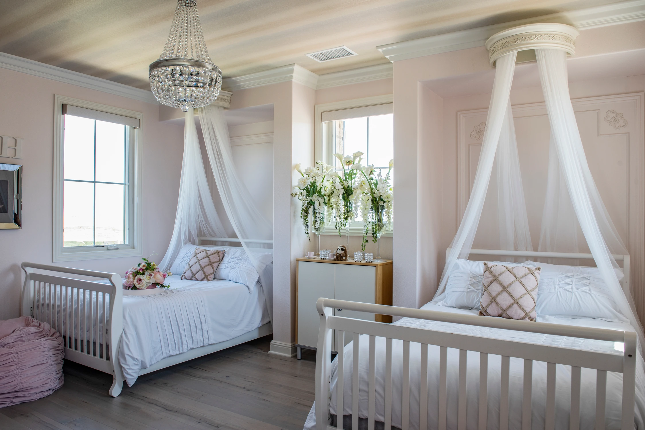 Pink nursery with two canopy beds, cribs, and crystal chandelier