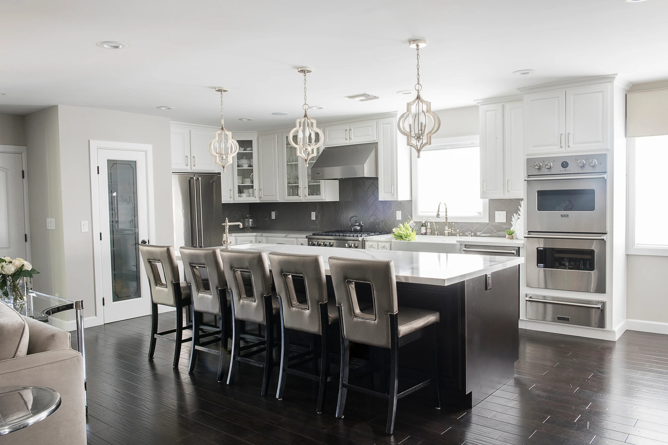 Kitchen island lined with dark stools beneath hanging lights