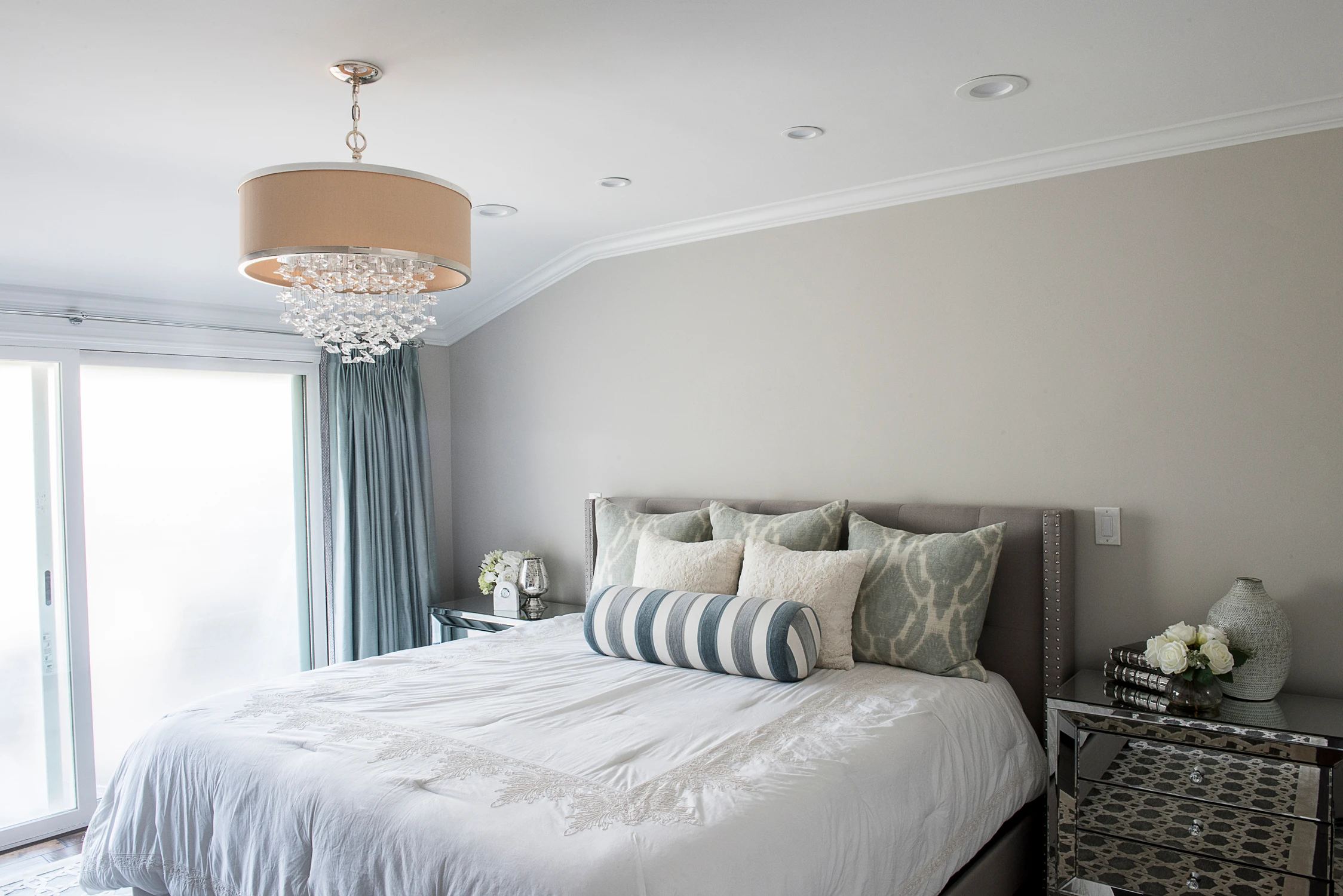 Bedroom with pale upholstered bed, blue drapery, and striped bolster pillow