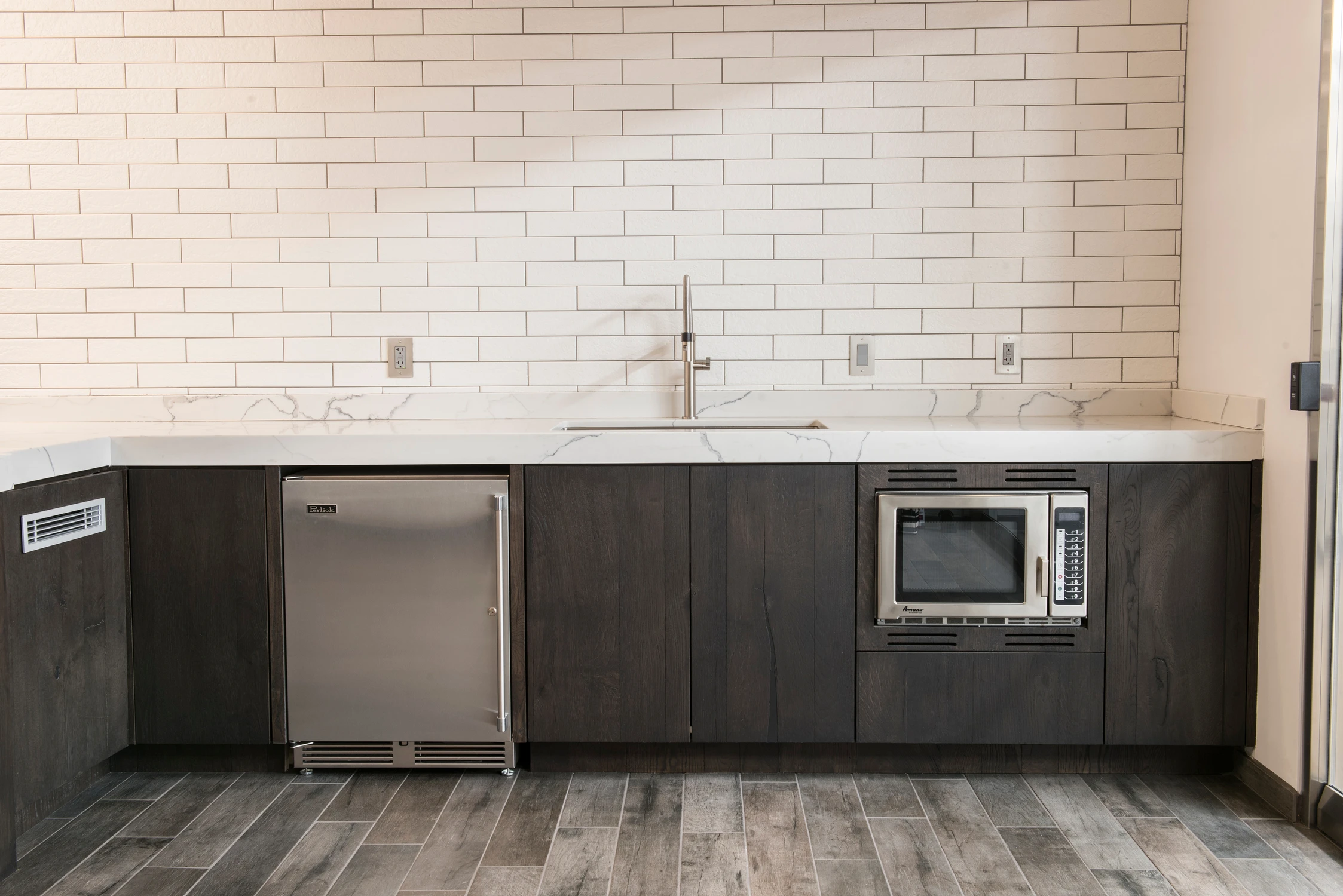 Dark wood kitchenette with white tile backsplash and built-in appliances