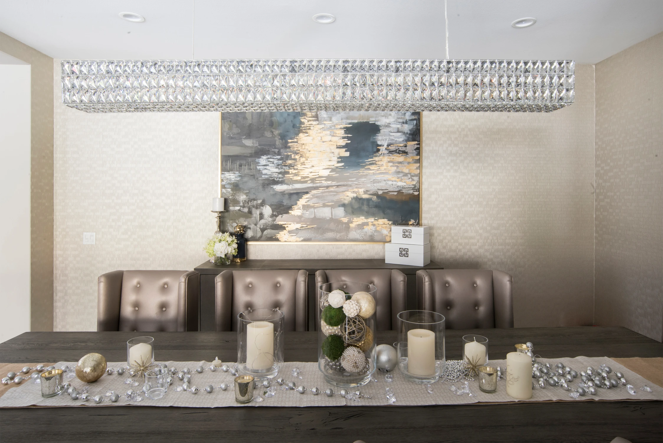 Formal dining table with long crystal chandelier and neutral upholstered chairs