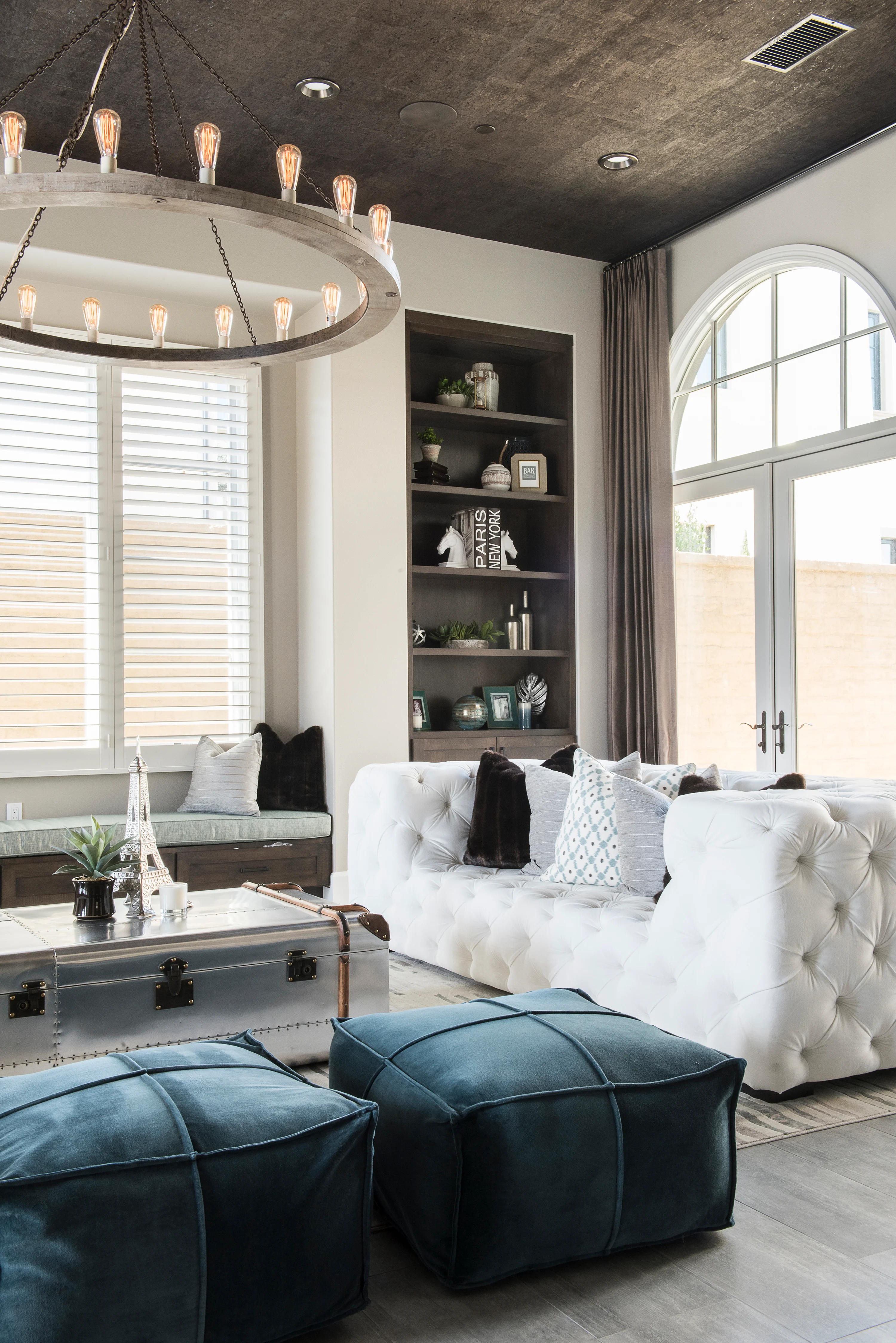 White tufted sofa and blue ottomans beneath an oversized circular chandelier