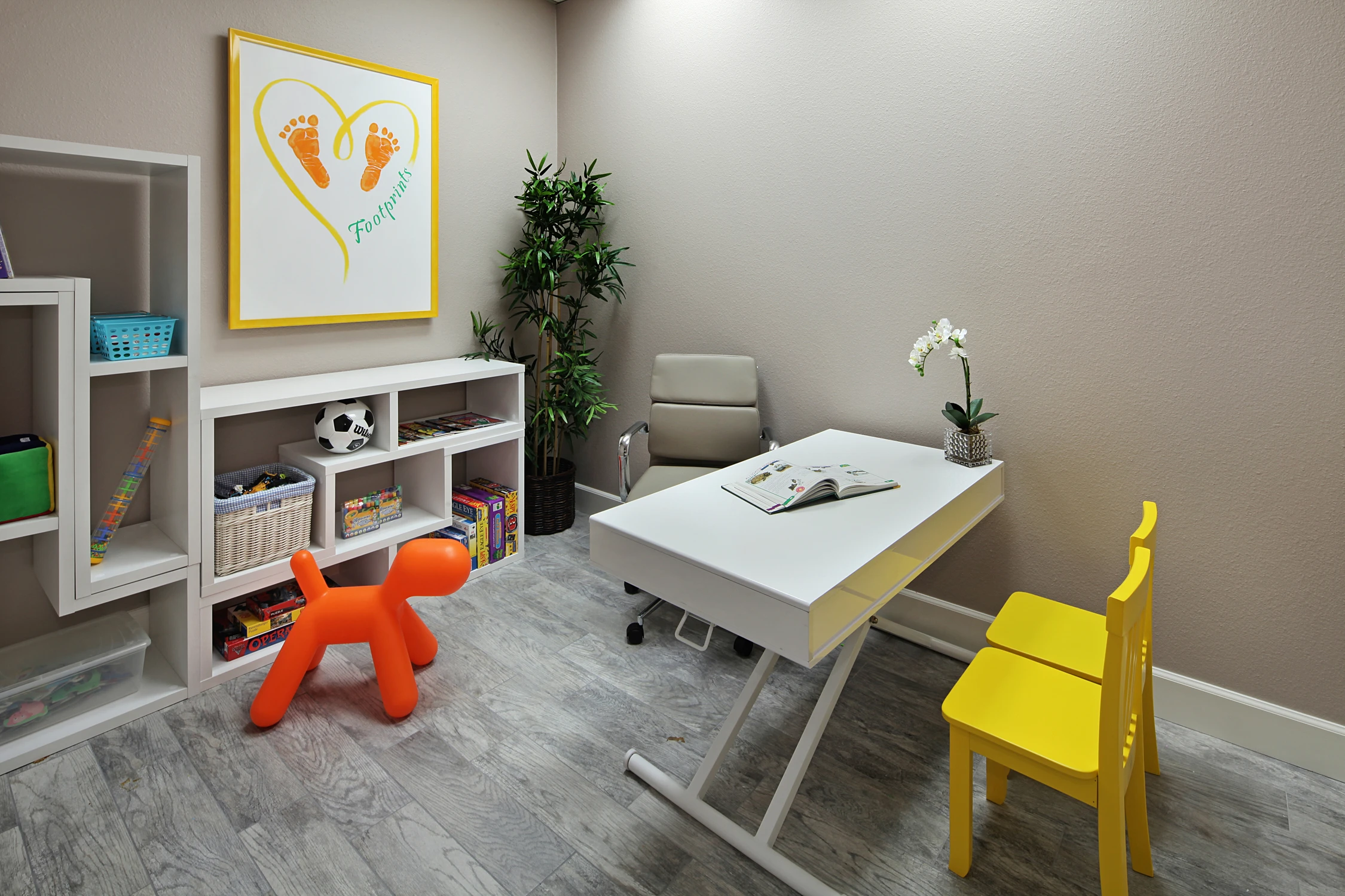 Small therapy room with yellow chairs, bookshelves, and play table