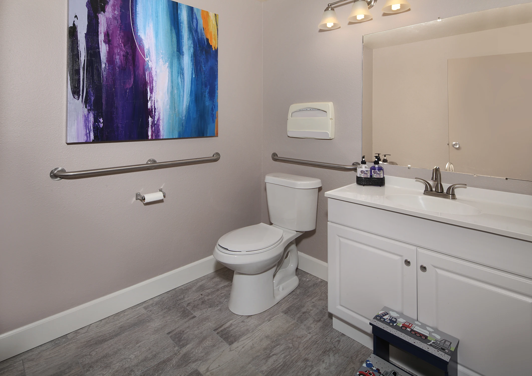 Accessible clinic restroom with white vanity and gray plank flooring