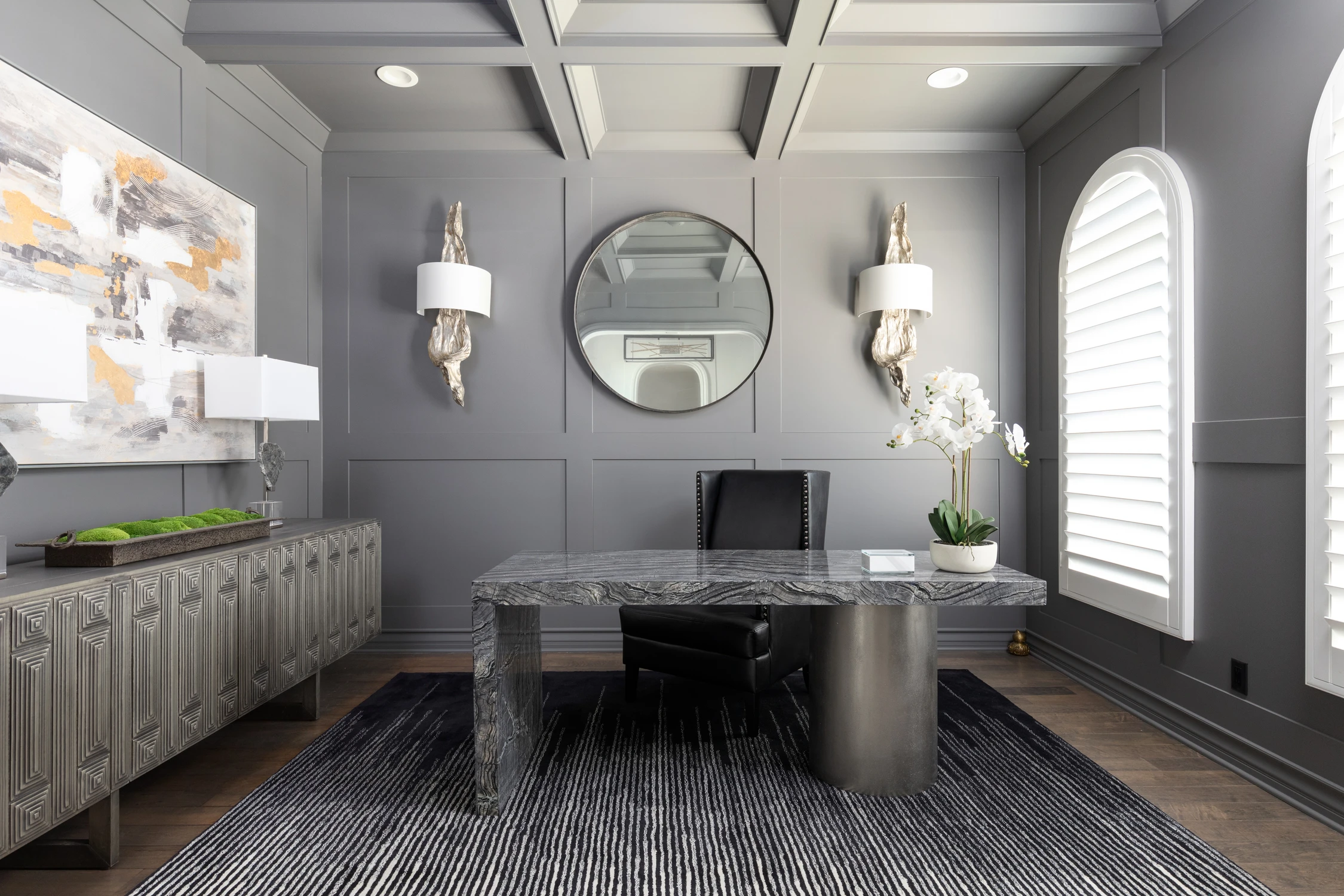 Dark paneled home office with a stone desk and round mirror