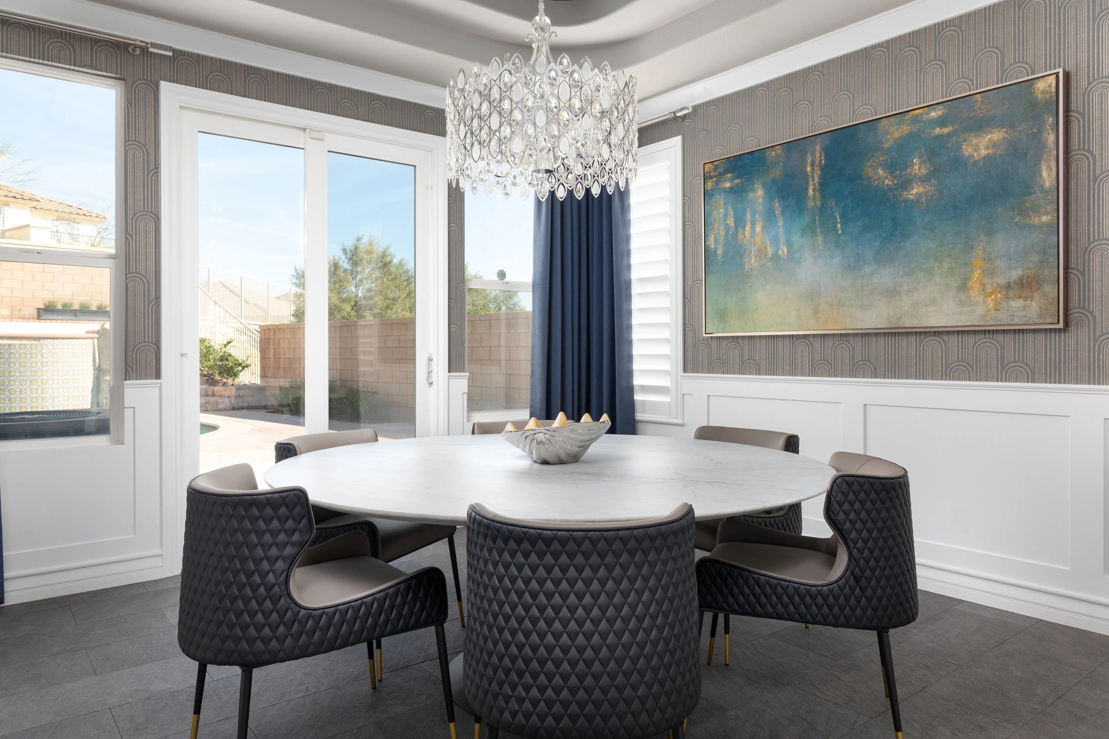 Dining table beneath a crystal chandelier and blue abstract artwork