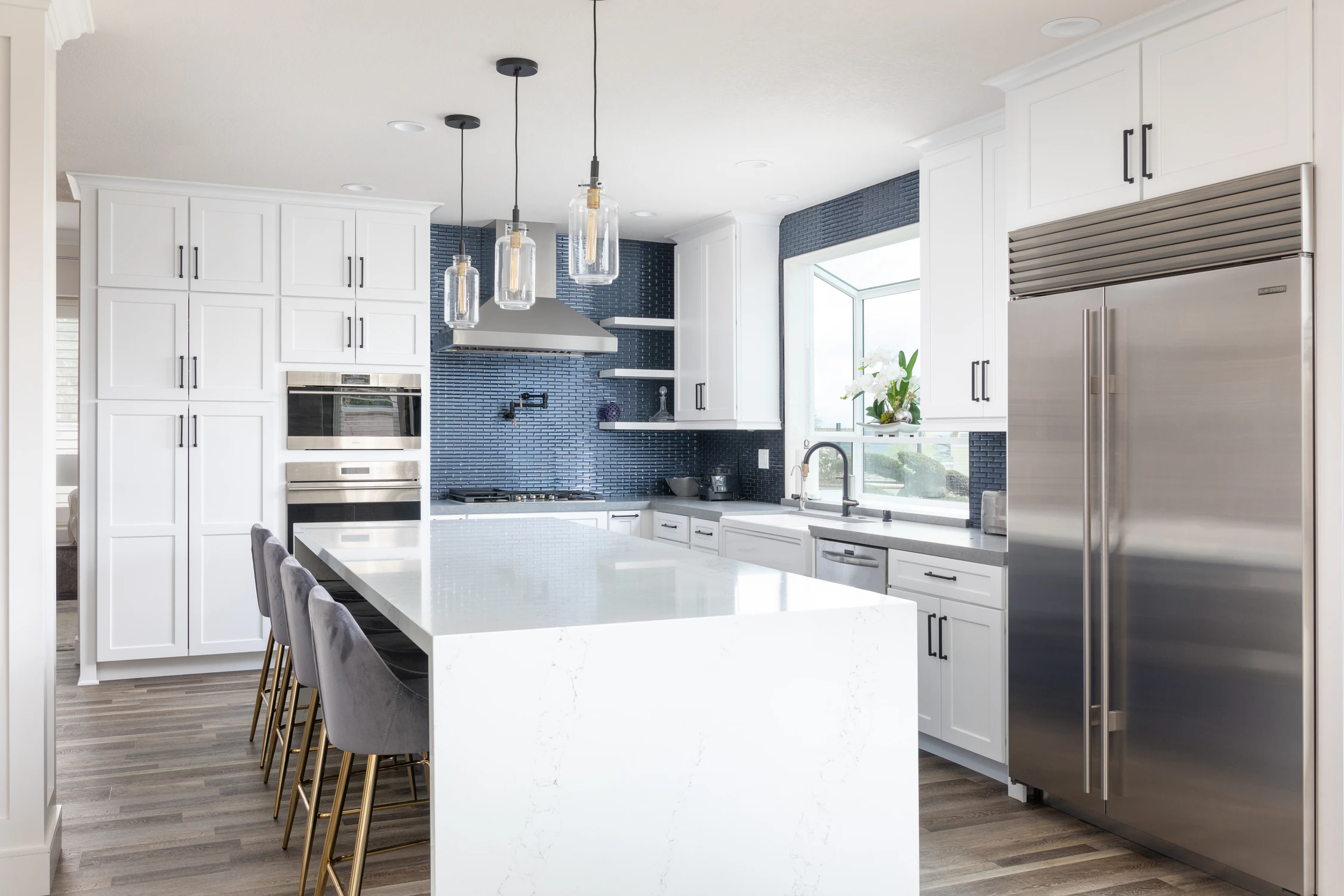 White kitchen with navy tile backsplash, waterfall island, and gray stools