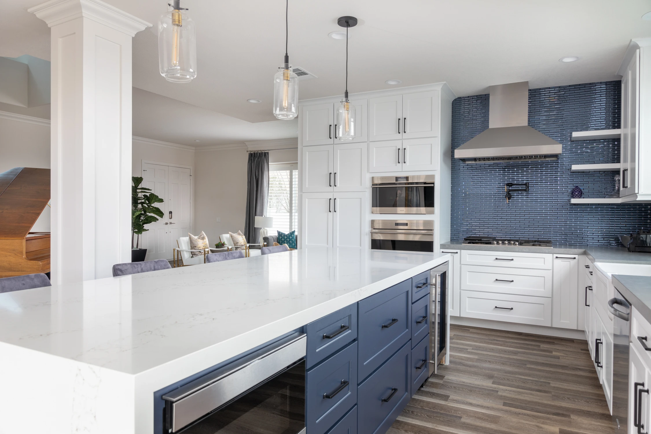 White kitchen with navy island, glass pendants, and blue tile backsplash