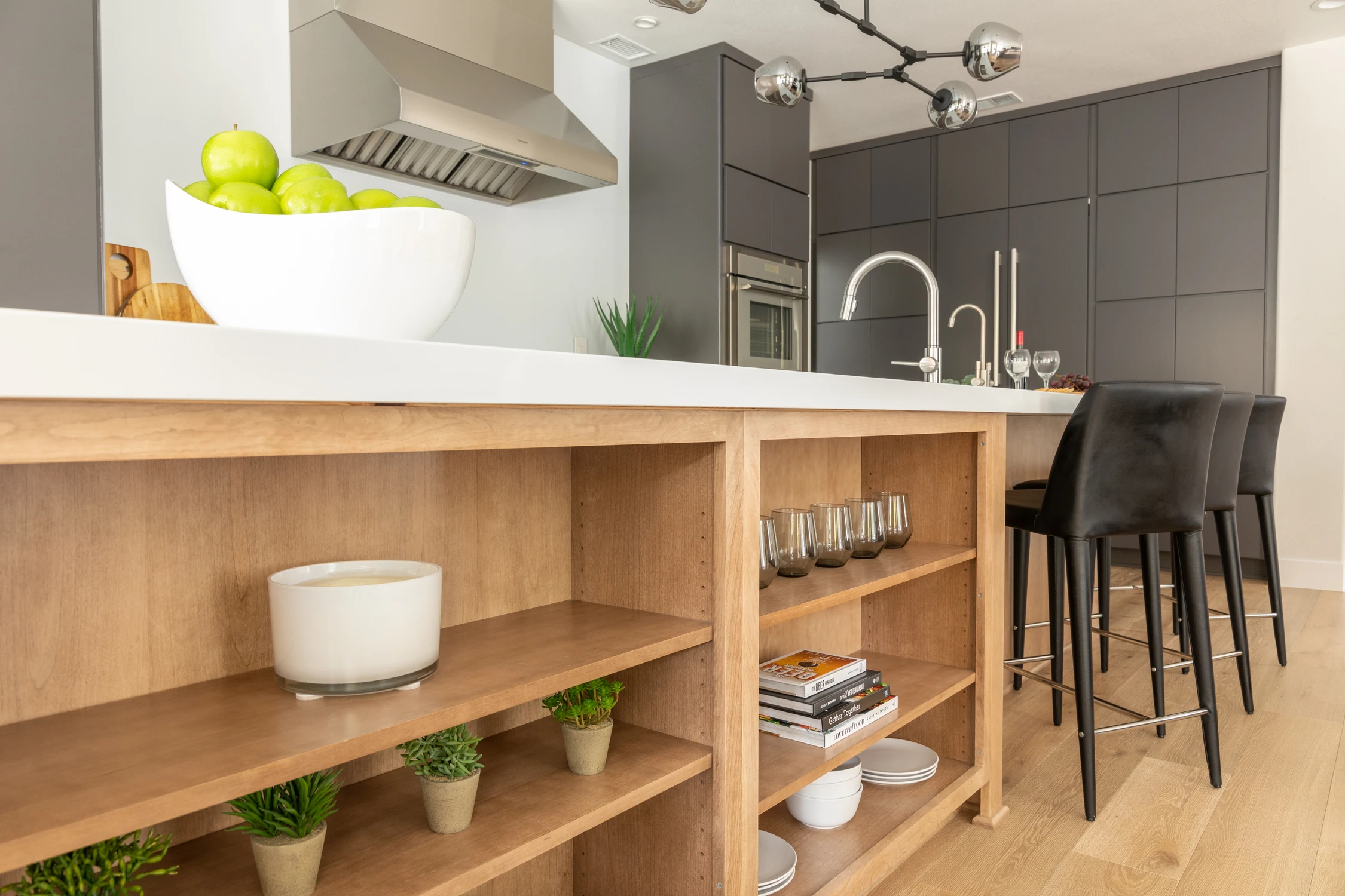 Open wood shelves beneath white kitchen counter beside black stool