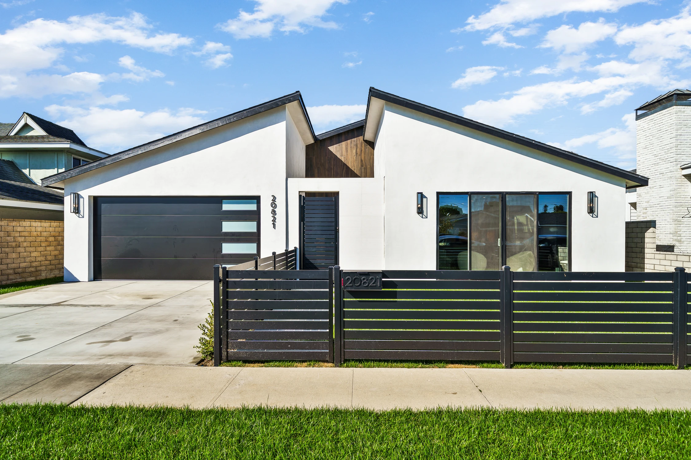 White modern home exterior with black garage door and horizontal fence