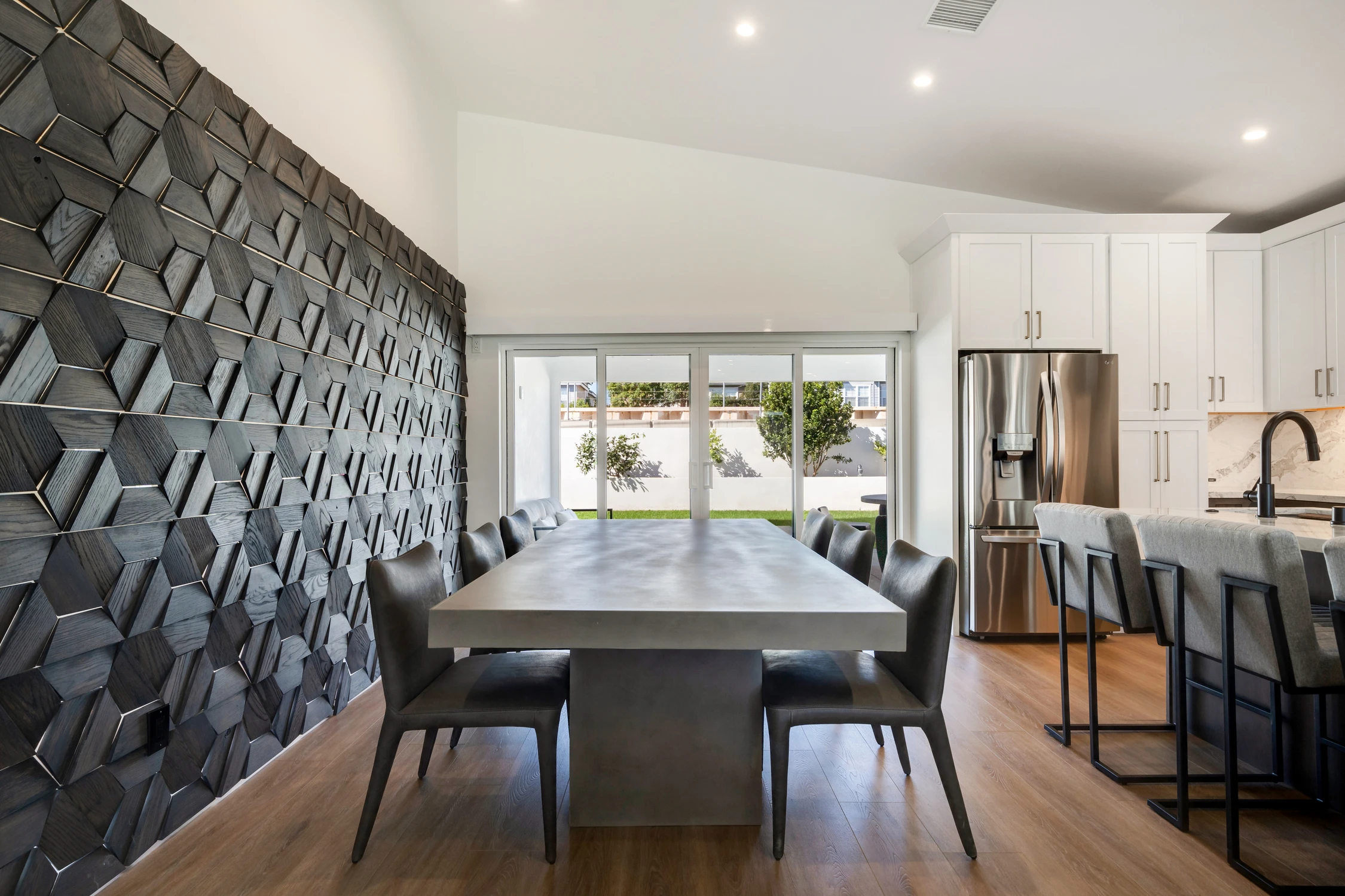 Dining table beside dimensional dark wood feature wall and kitchen island