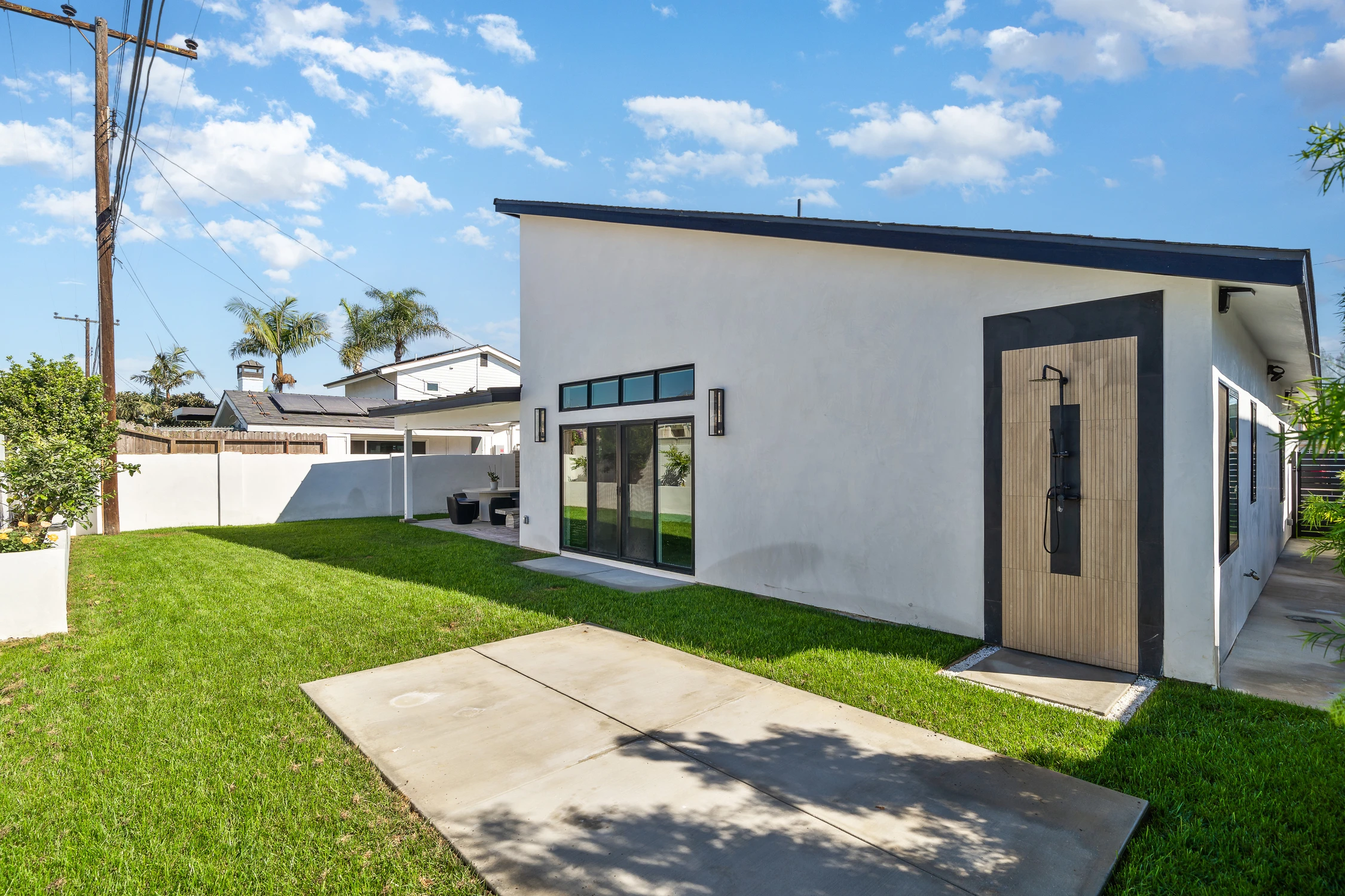 Backyard of white modern home with lawn, covered patio, and outdoor shower