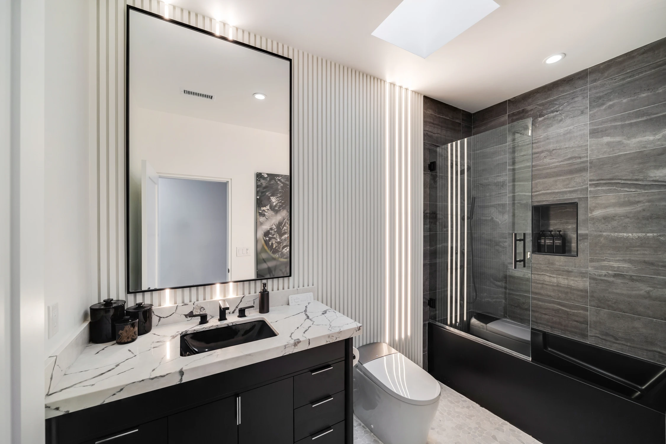 Bathroom with black vanity, marble counter, and gray tile shower