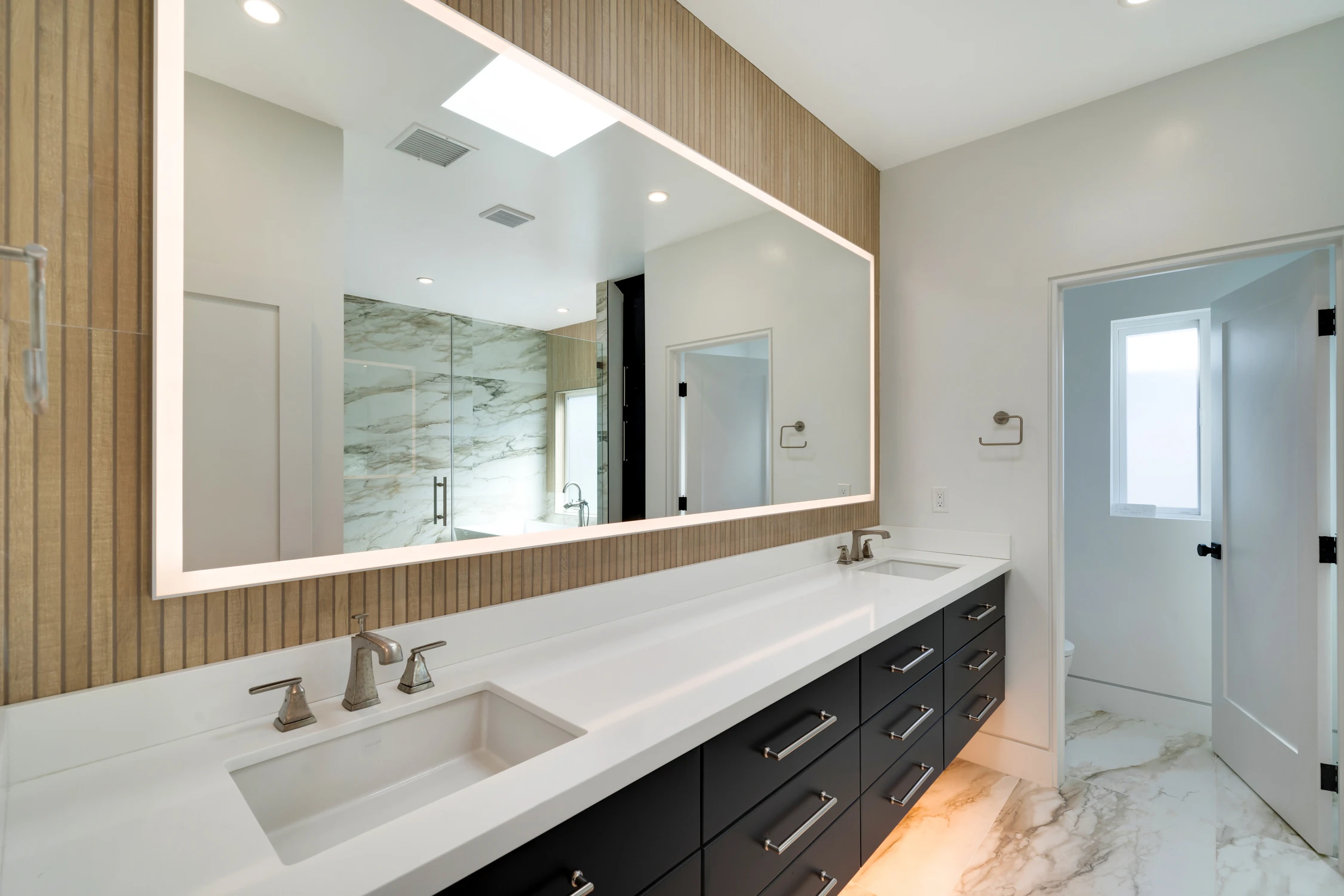 Bathroom double vanity with black cabinetry and illuminated mirror