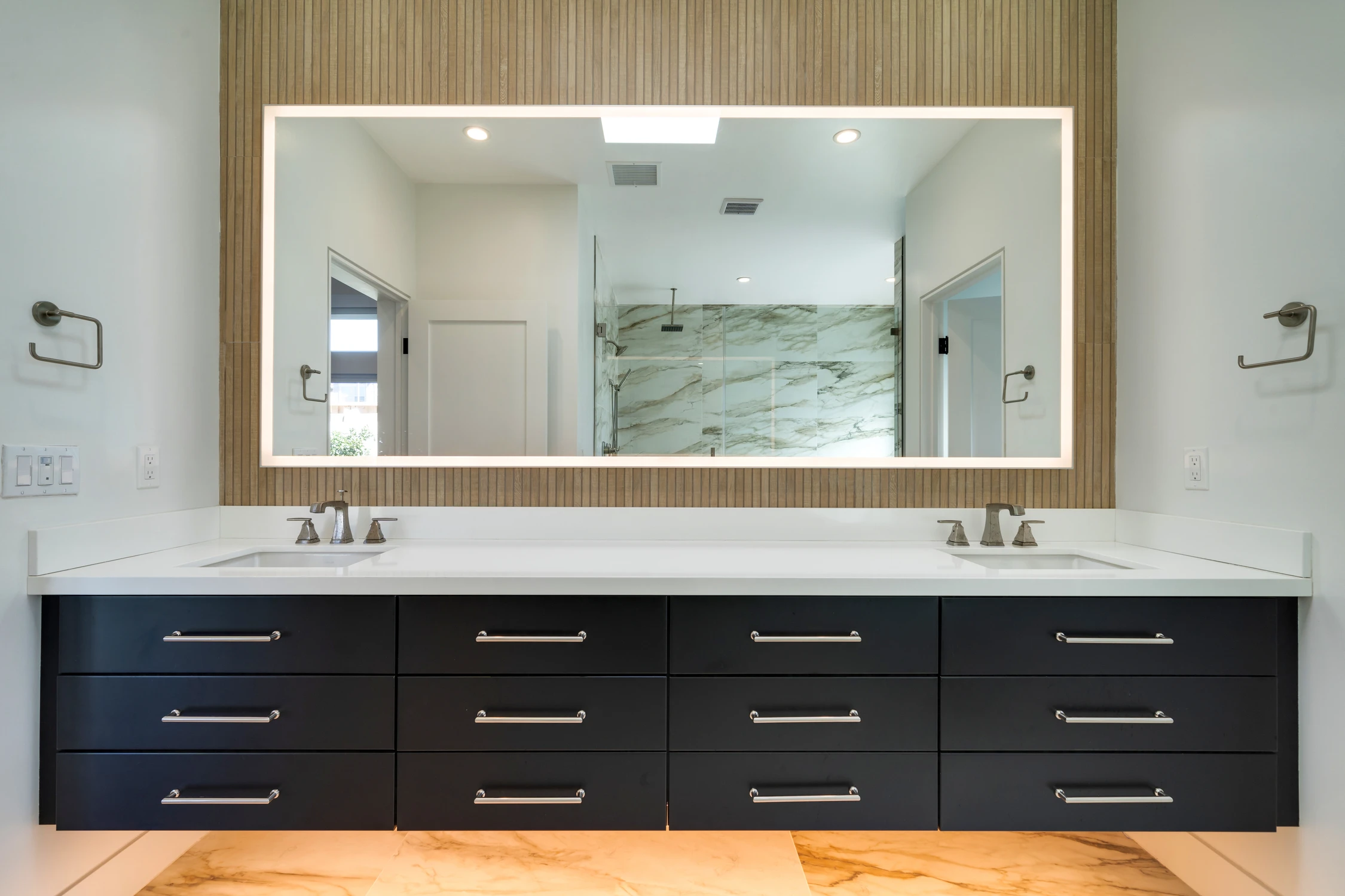 Bathroom double vanity with black drawers and wood-framed illuminated mirror