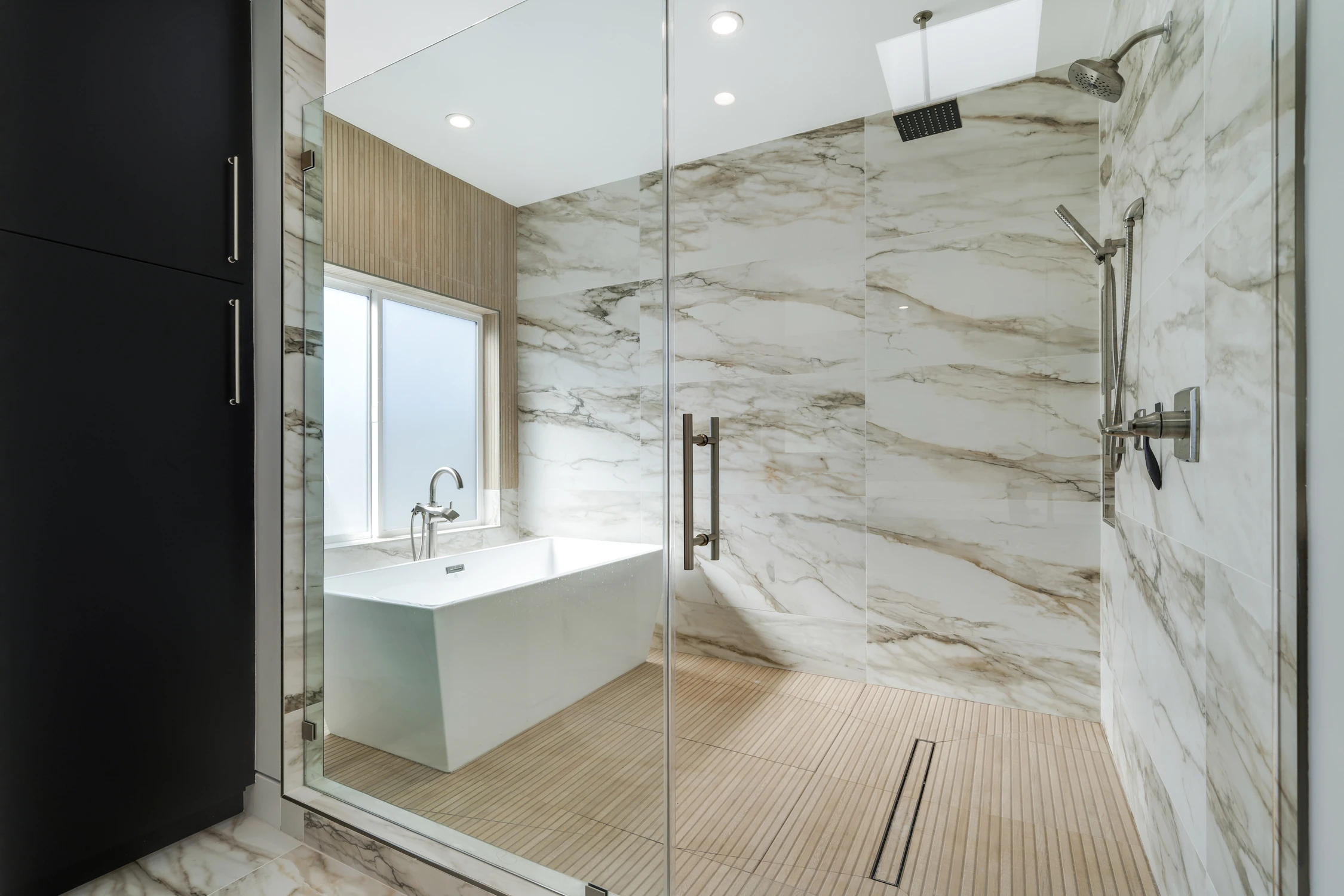 Marble bathroom shower and freestanding tub with wood tile floor
