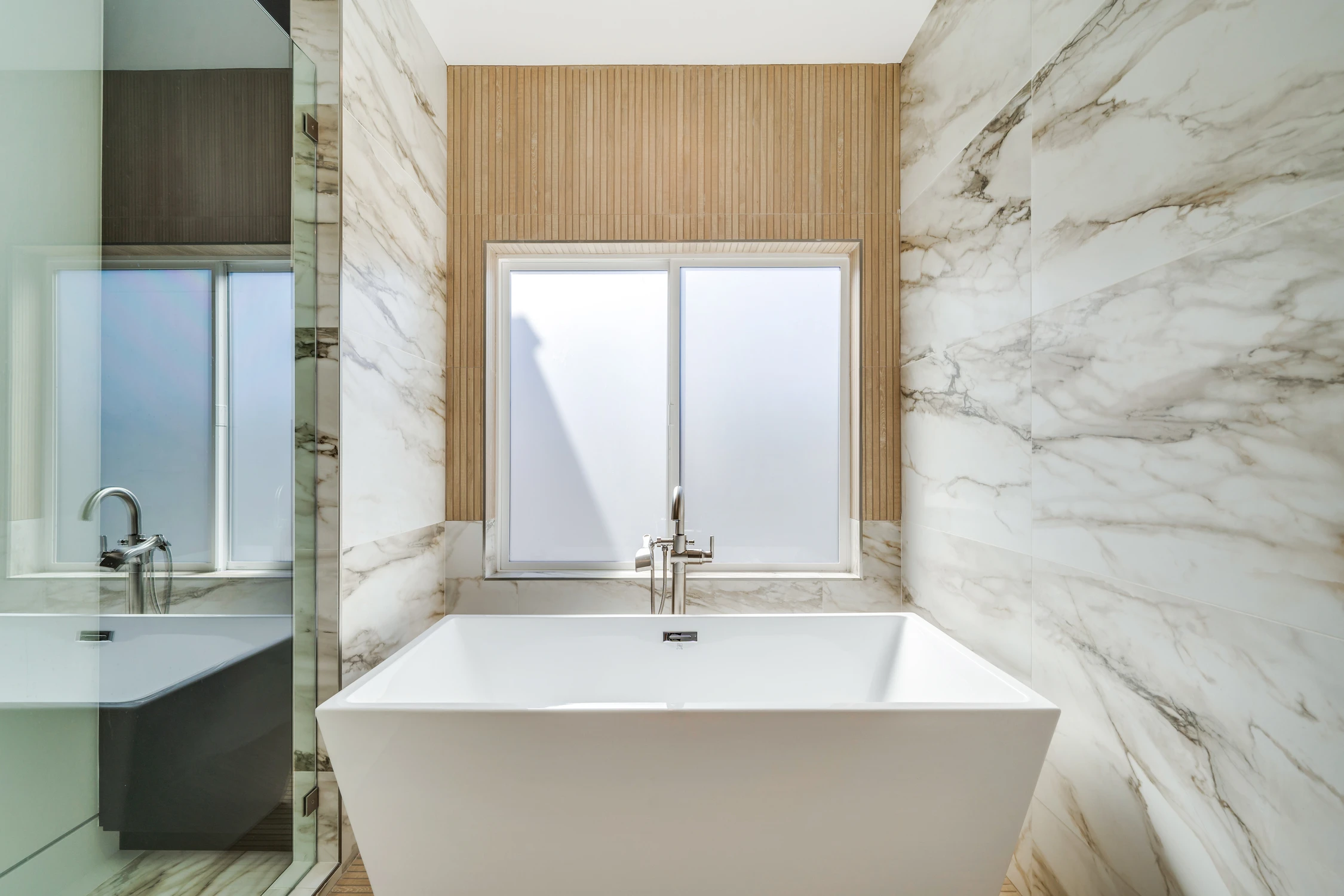 Freestanding bathtub beside marble shower and frosted window