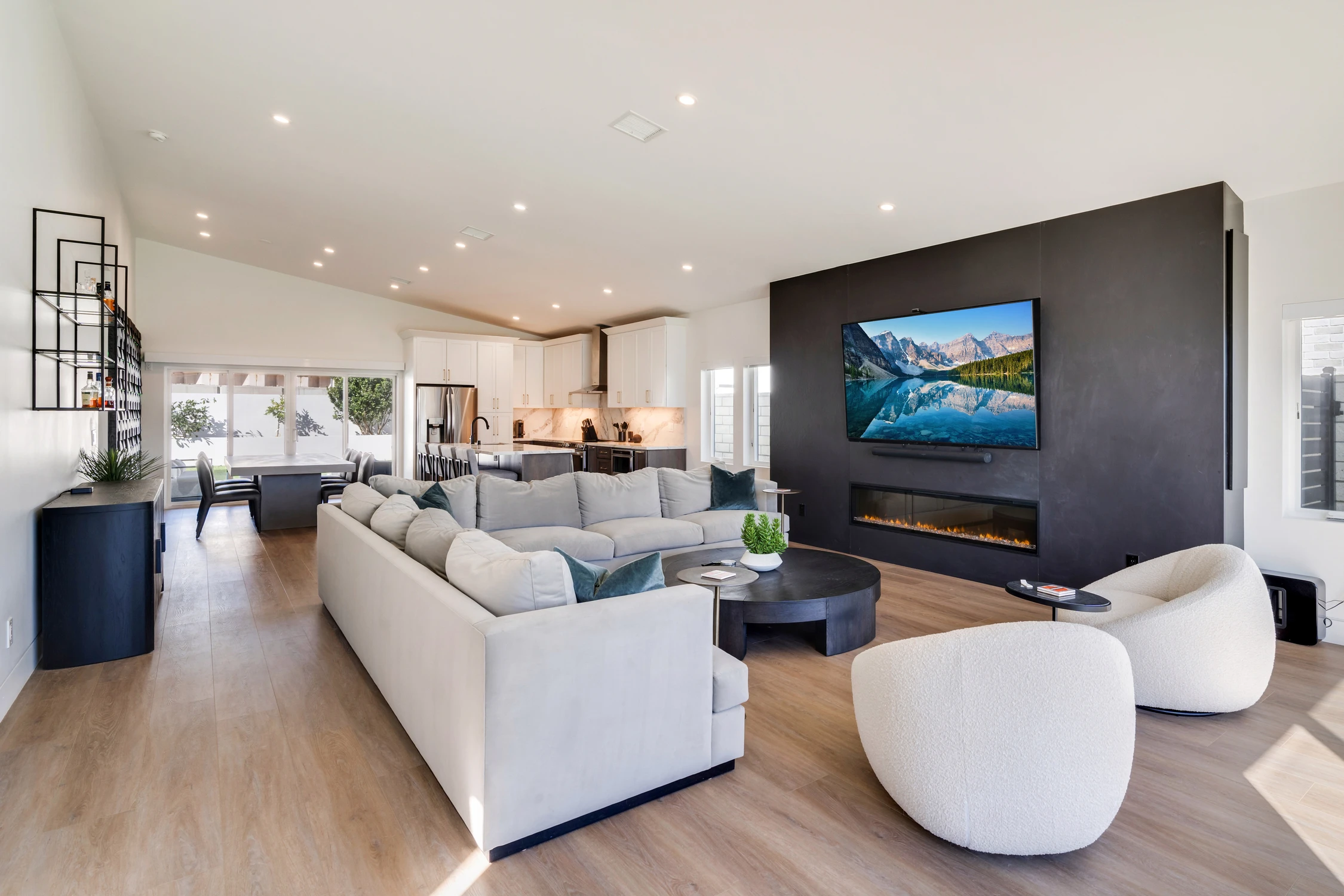 Open living room with white sectional, black media wall, and kitchen