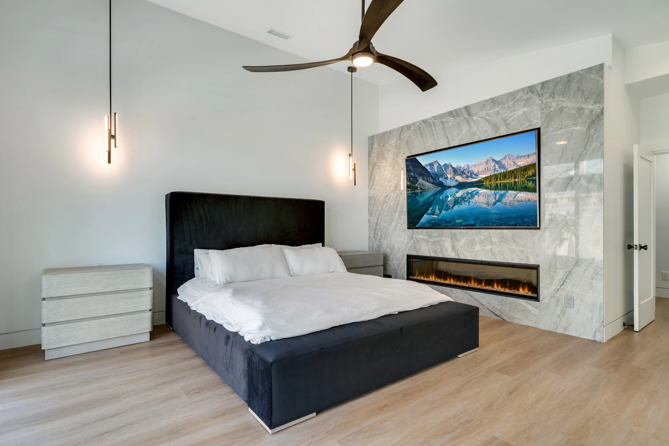 Primary bedroom with black upholstered bed, marble fireplace, and television