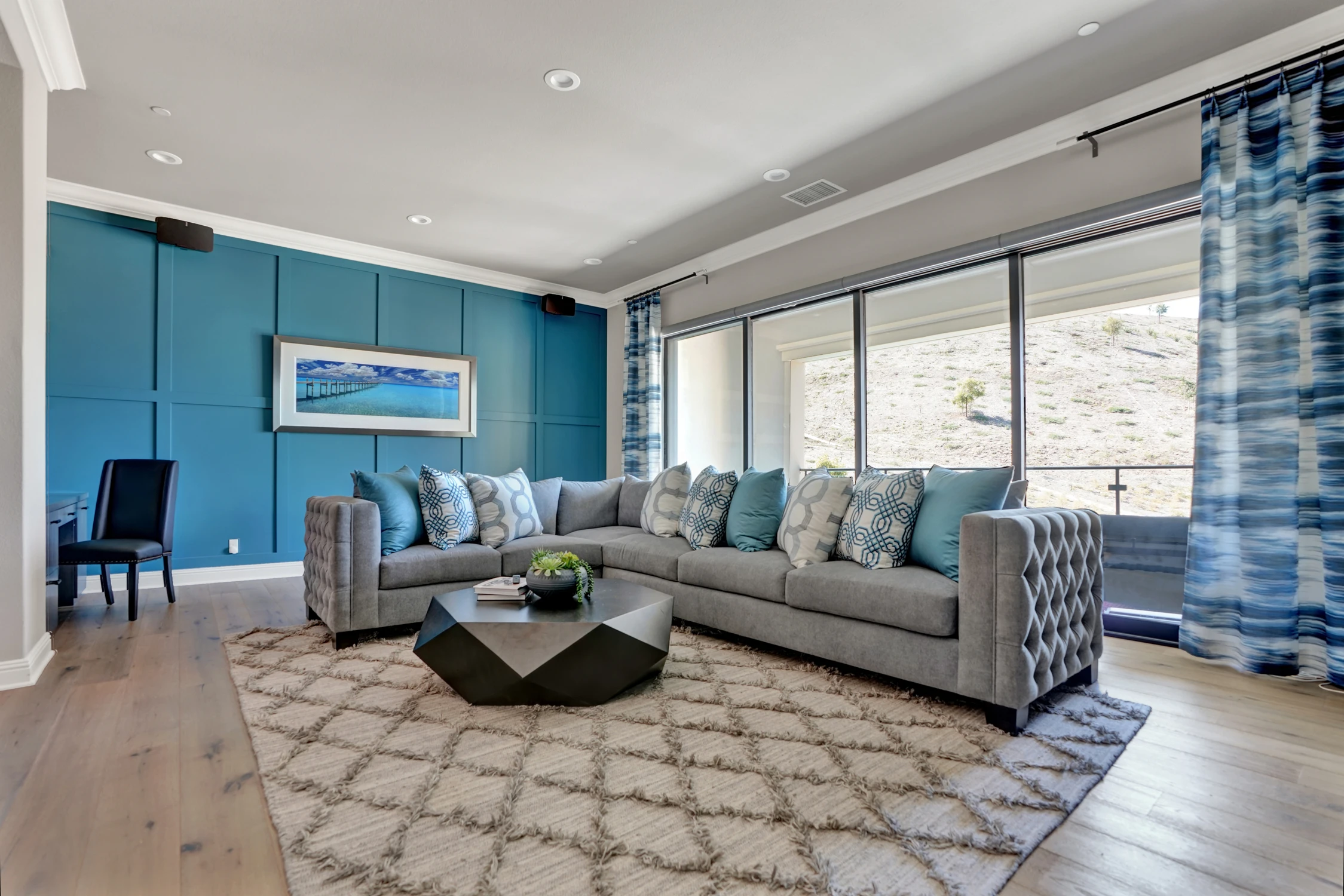 Living room with blue paneled walls, gray sofa, and wide windows