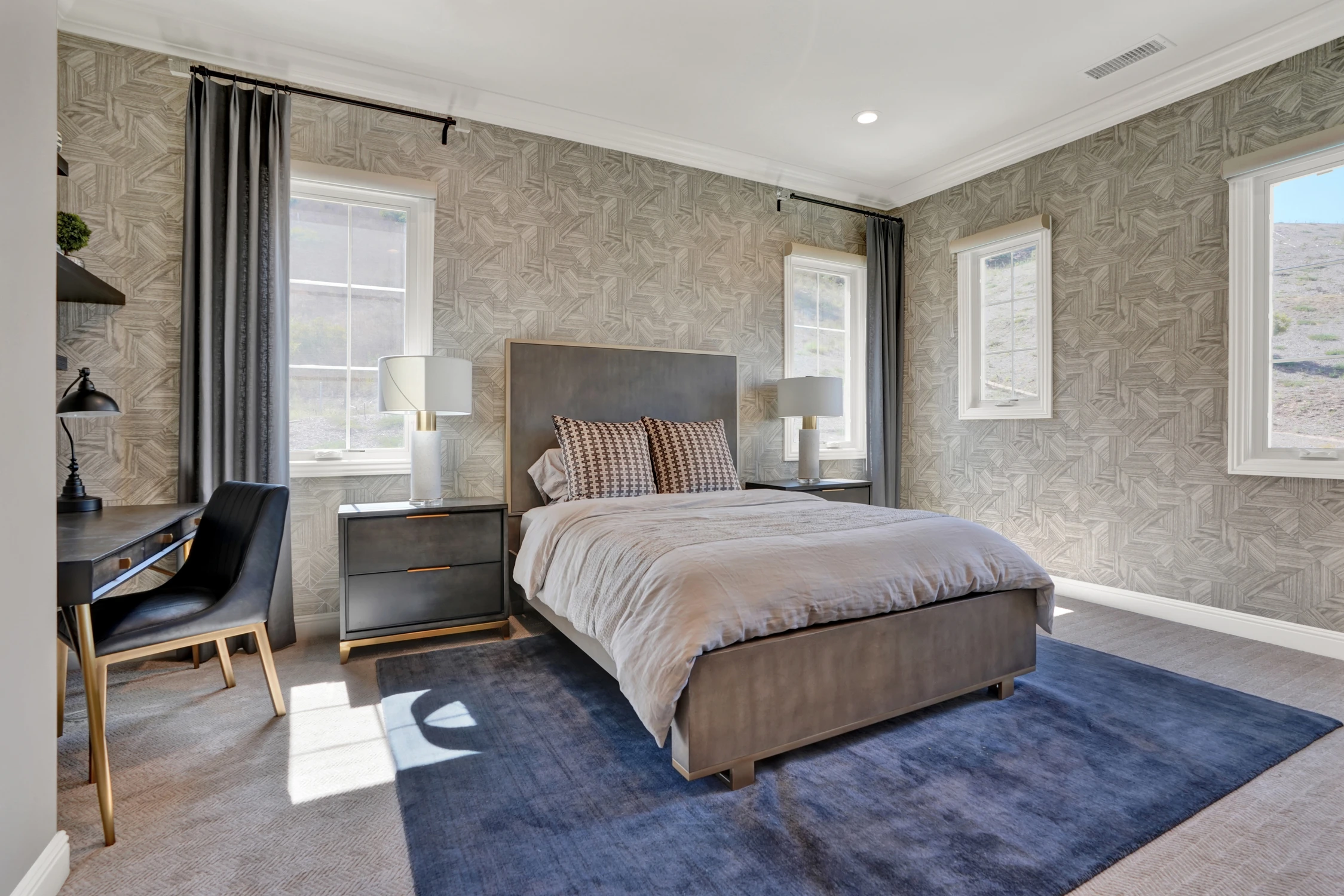 Bedroom with gray upholstered bed, blue rug, and black desk