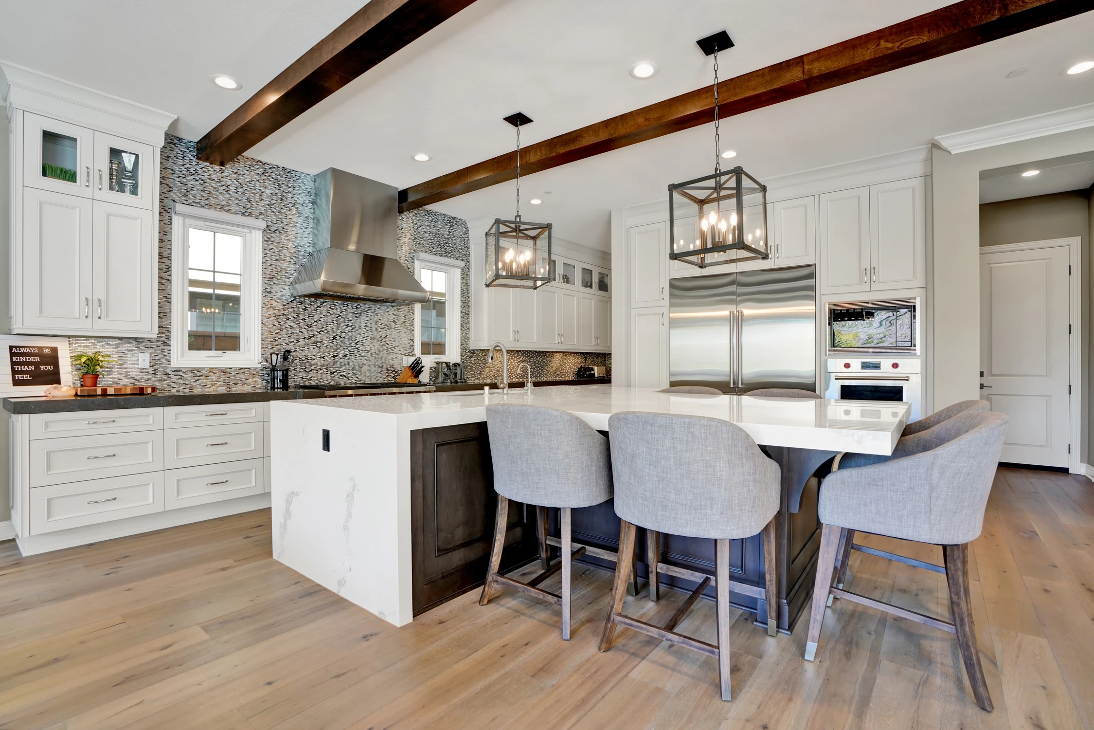White kitchen with dark island, upholstered stools, and exposed beams
