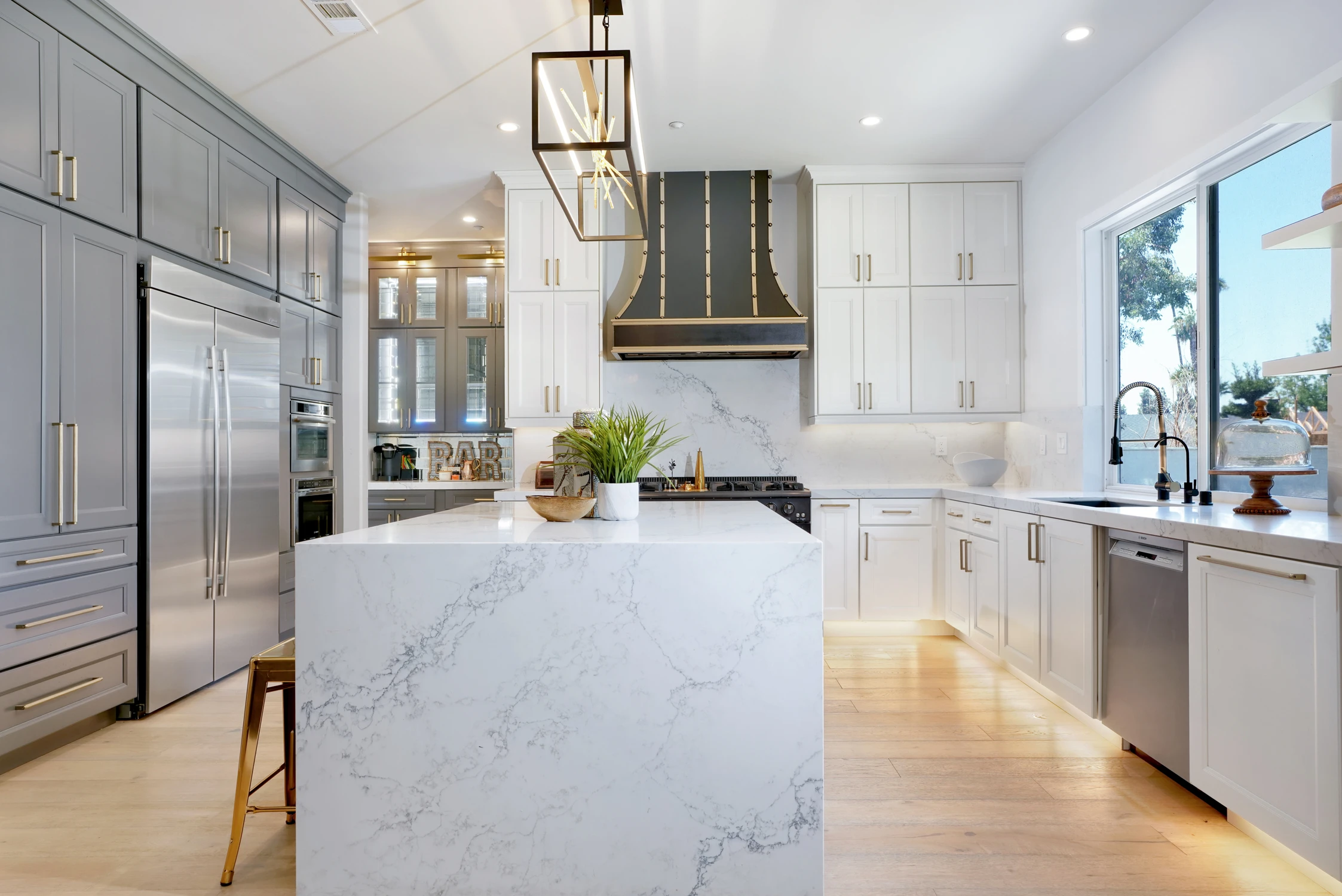 White and gray kitchen with marble island, dark hood, and brass stools
