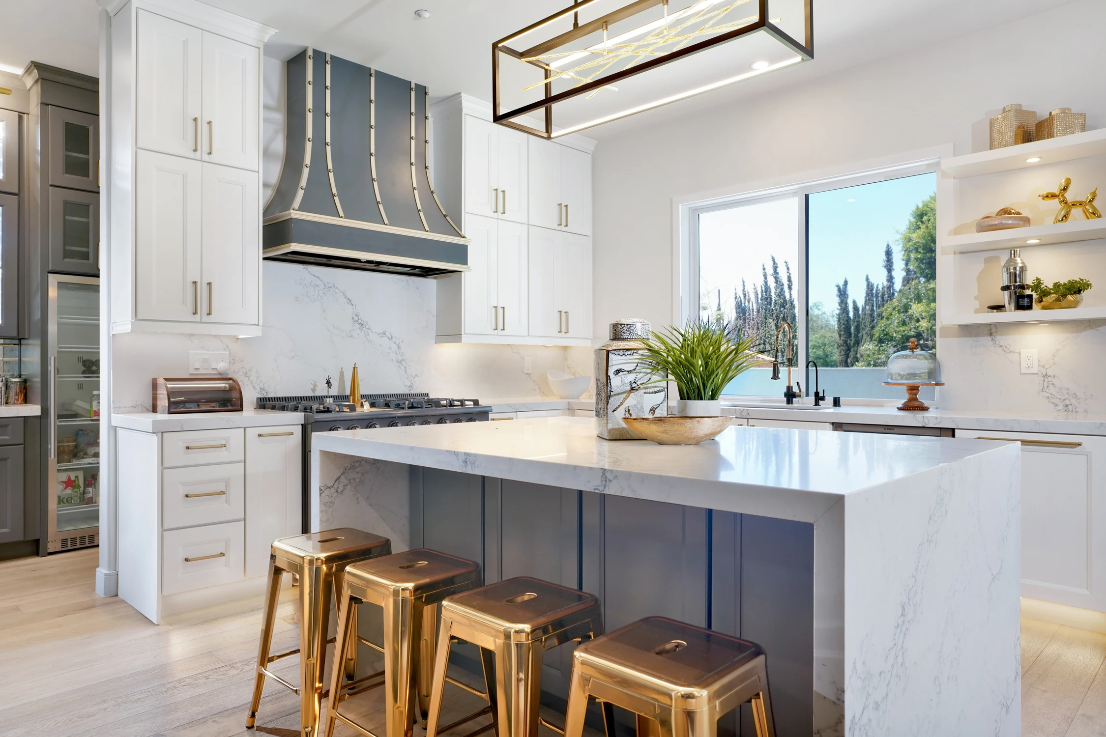 Kitchen island with brass stools, gray cabinetry, and black range hood