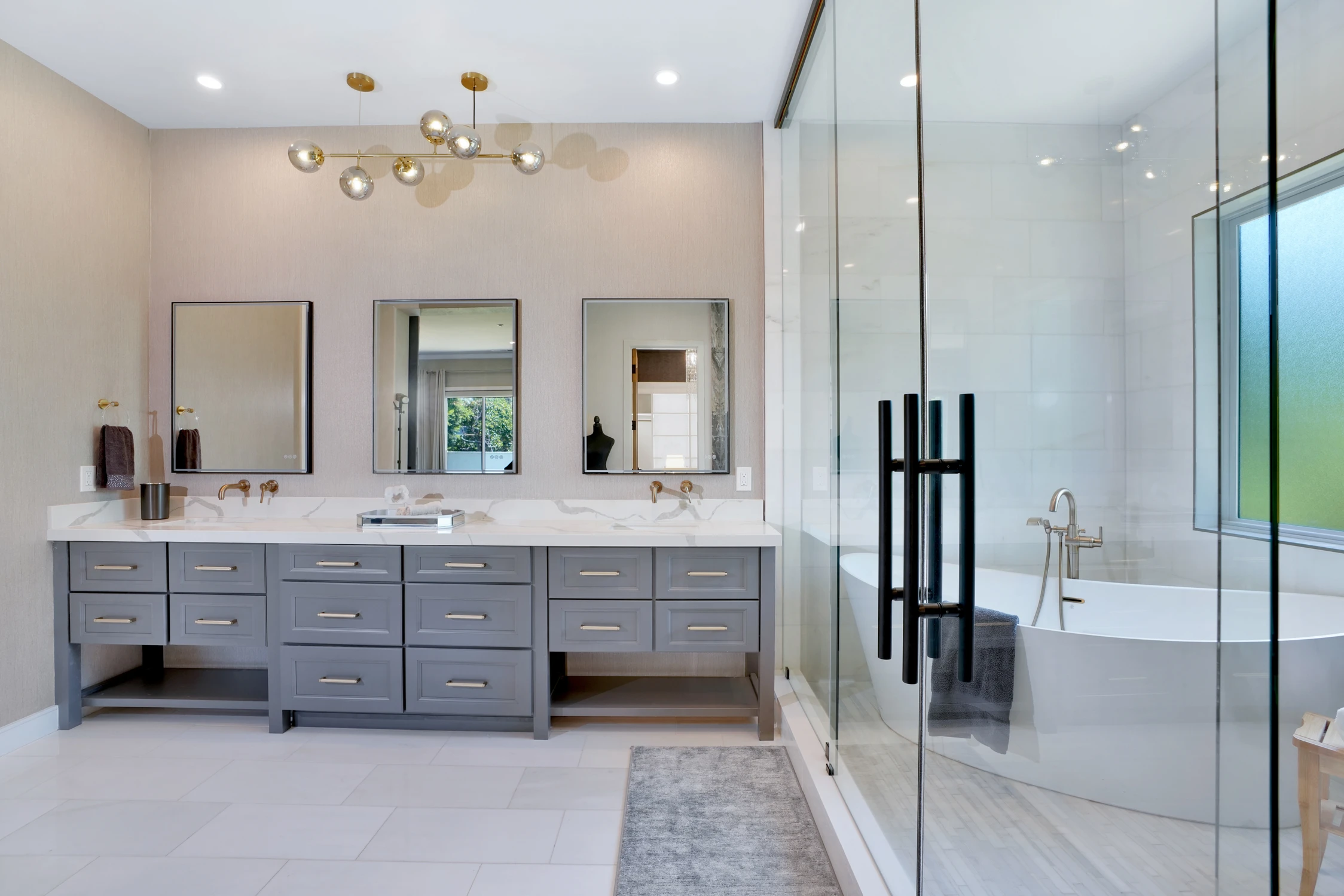 Master bathroom vanity with gray drawers, round mirror, and freestanding tub
