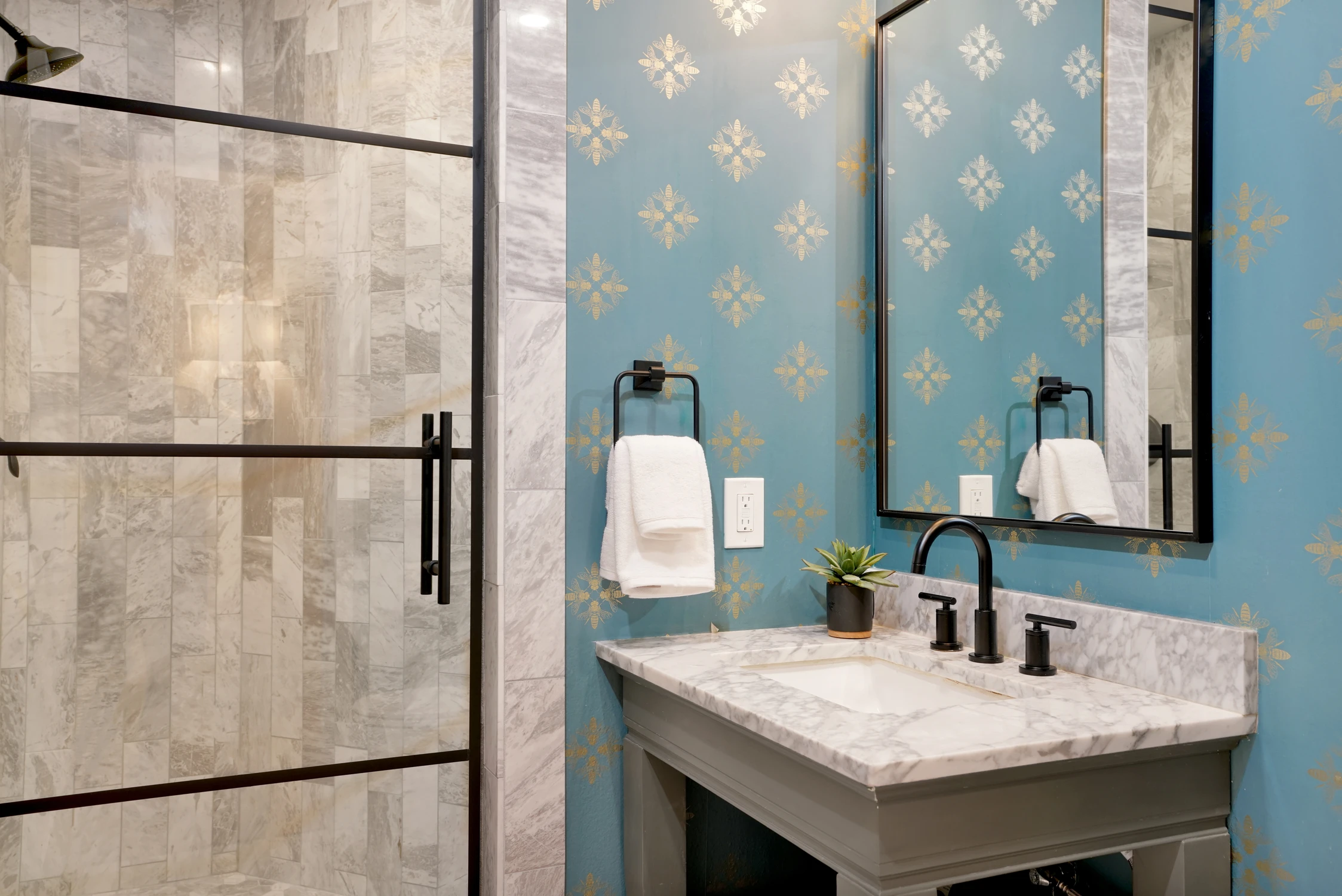 Bathroom with blue patterned wall, small wood vanity, and black faucet